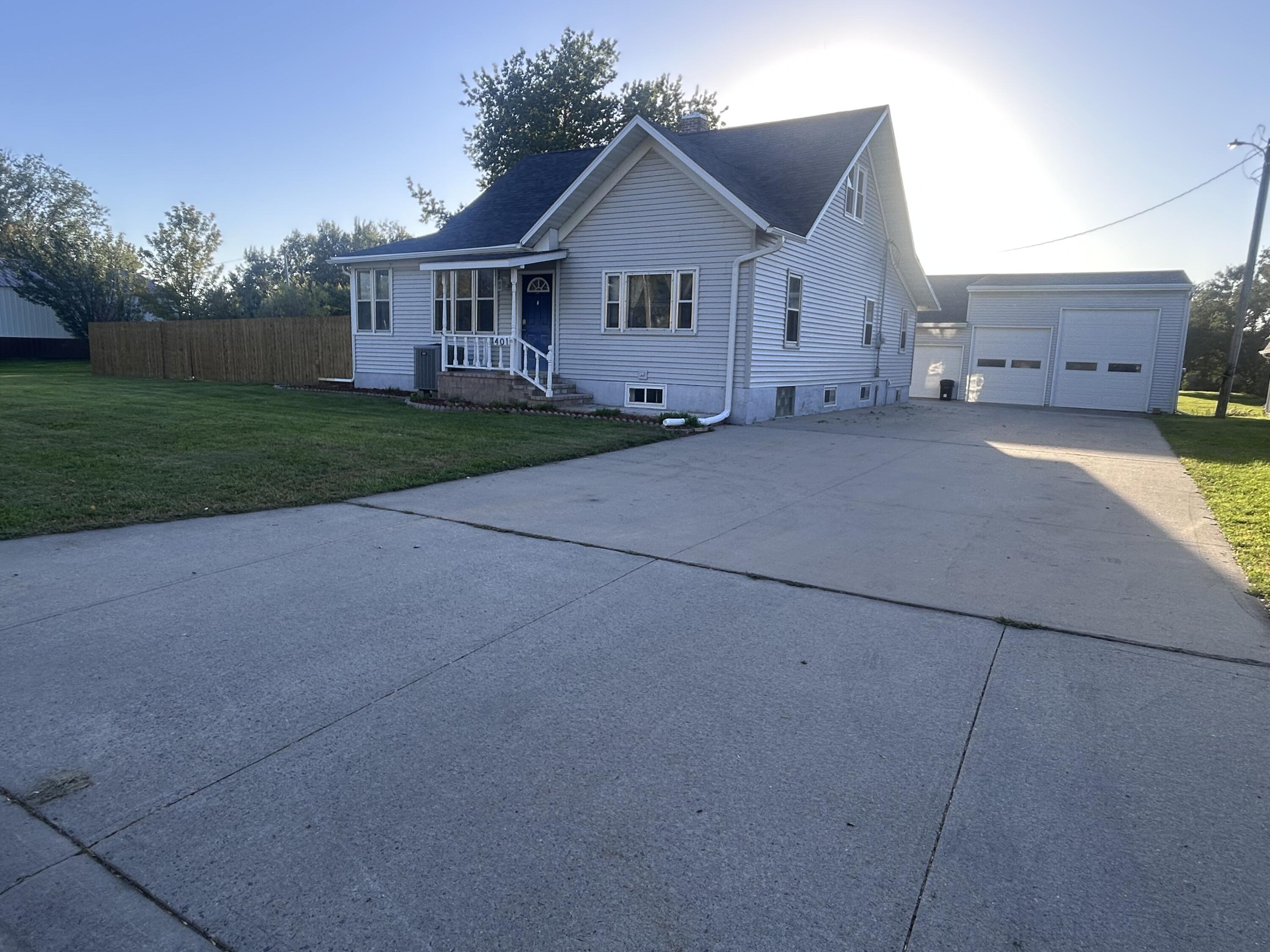 Light-colored house with a covered porch and detached garage beside a broad concrete driveway.