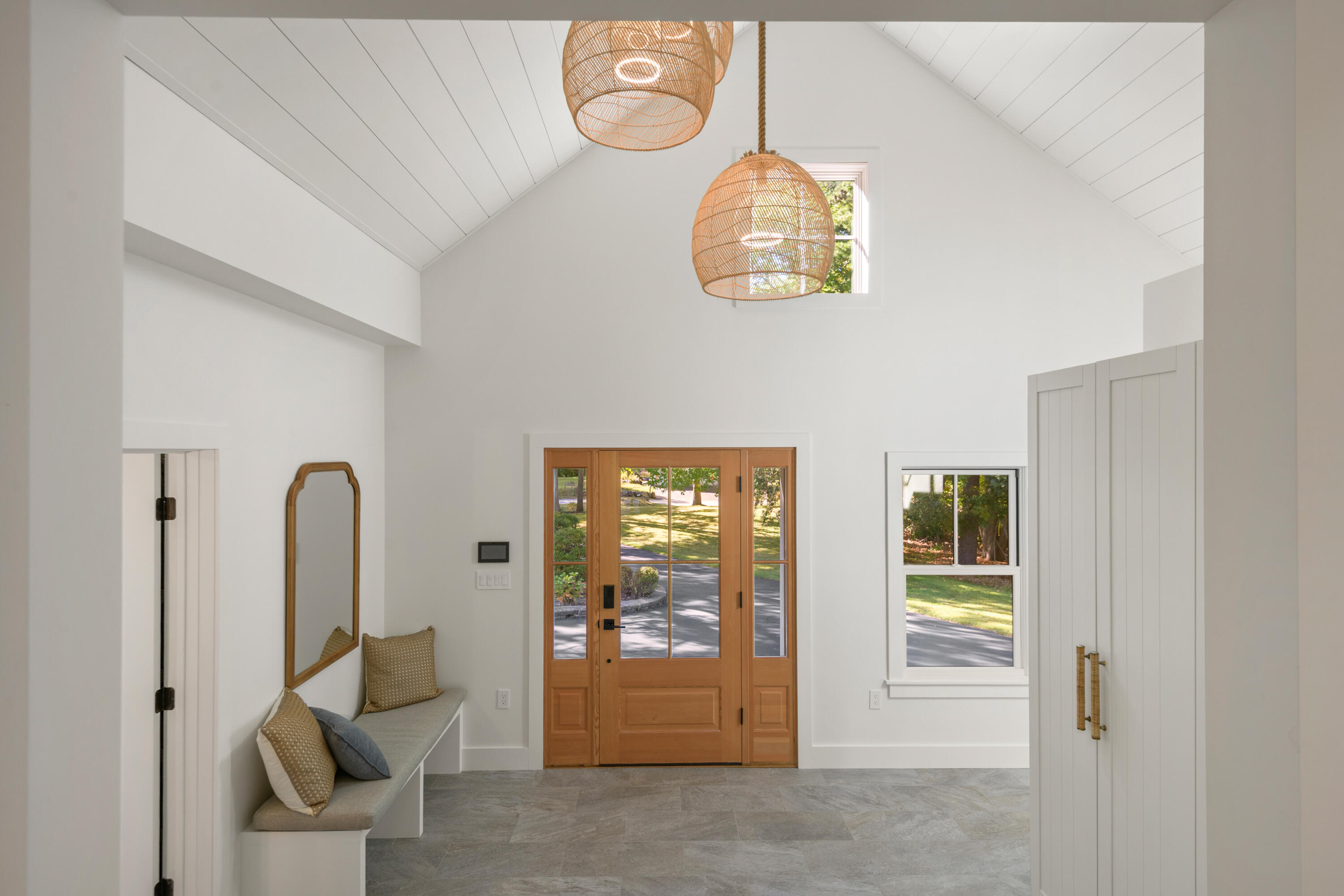 Bright entryway with a vaulted ceiling, woven pendant lights, wood-and-glass front door, and built-in bench.