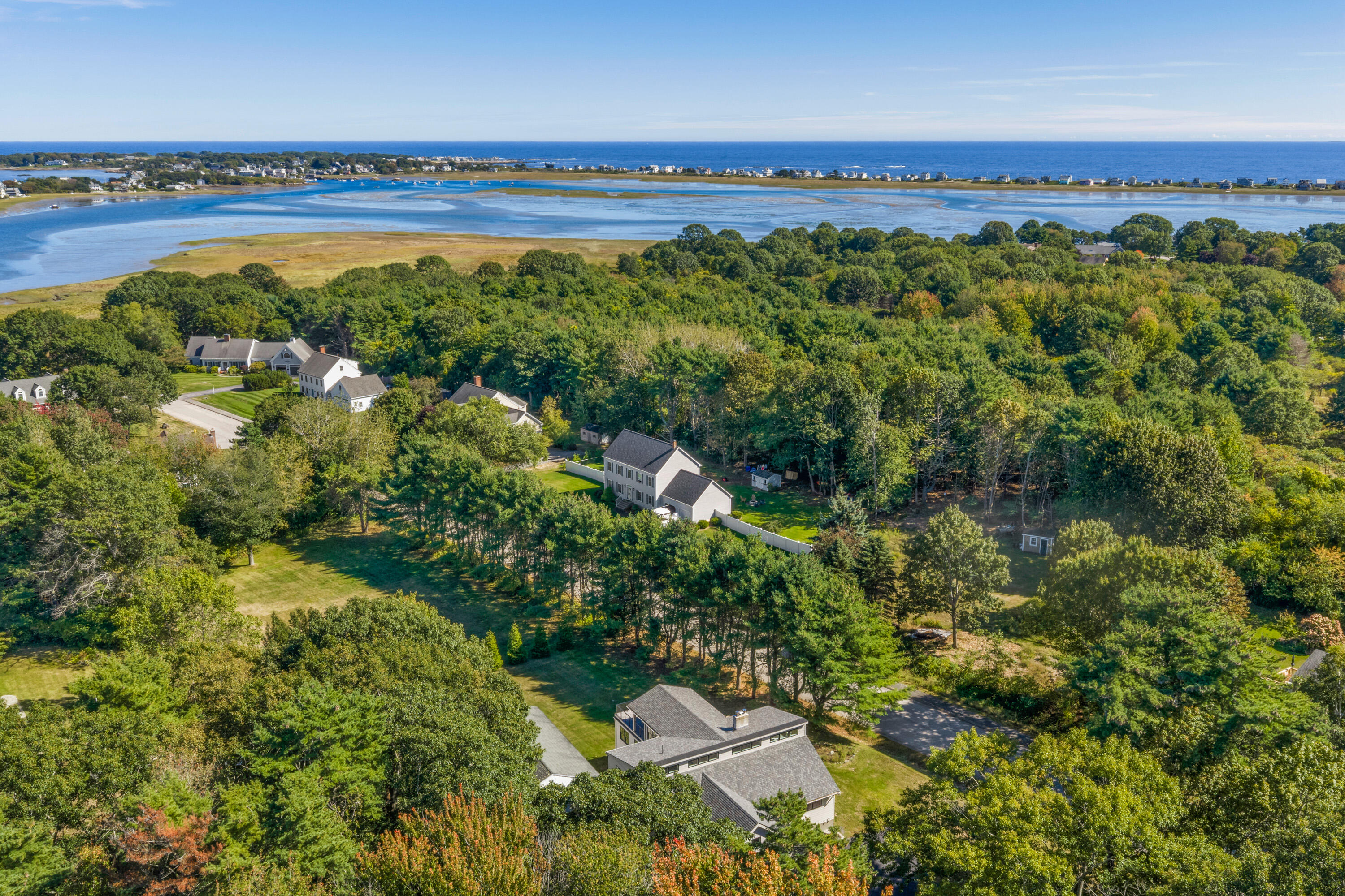 Aerial view of a home among trees, with a tidal inlet and ocean beyond.