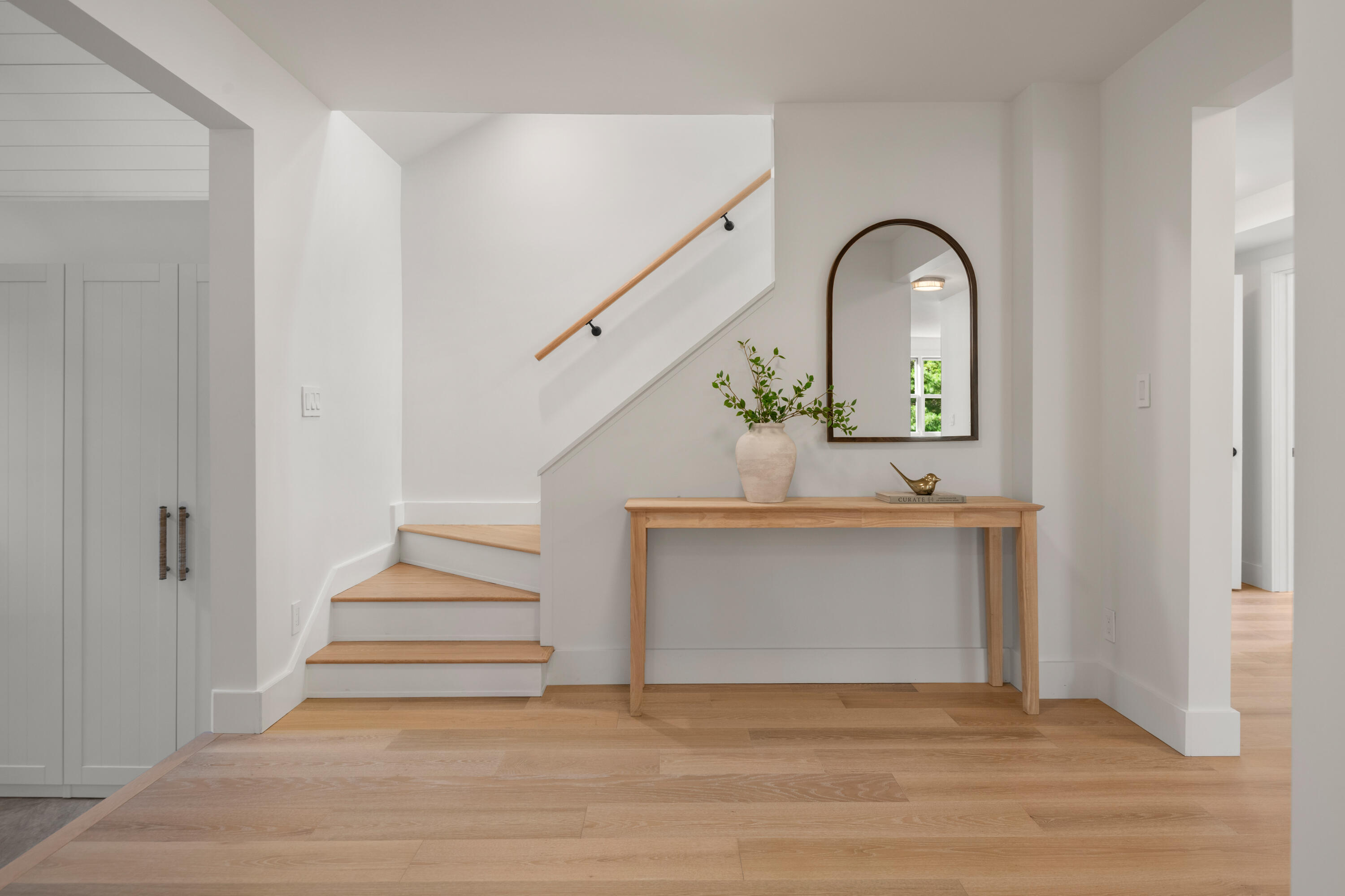 Bright entryway with a wood staircase, arched mirror, and console table.