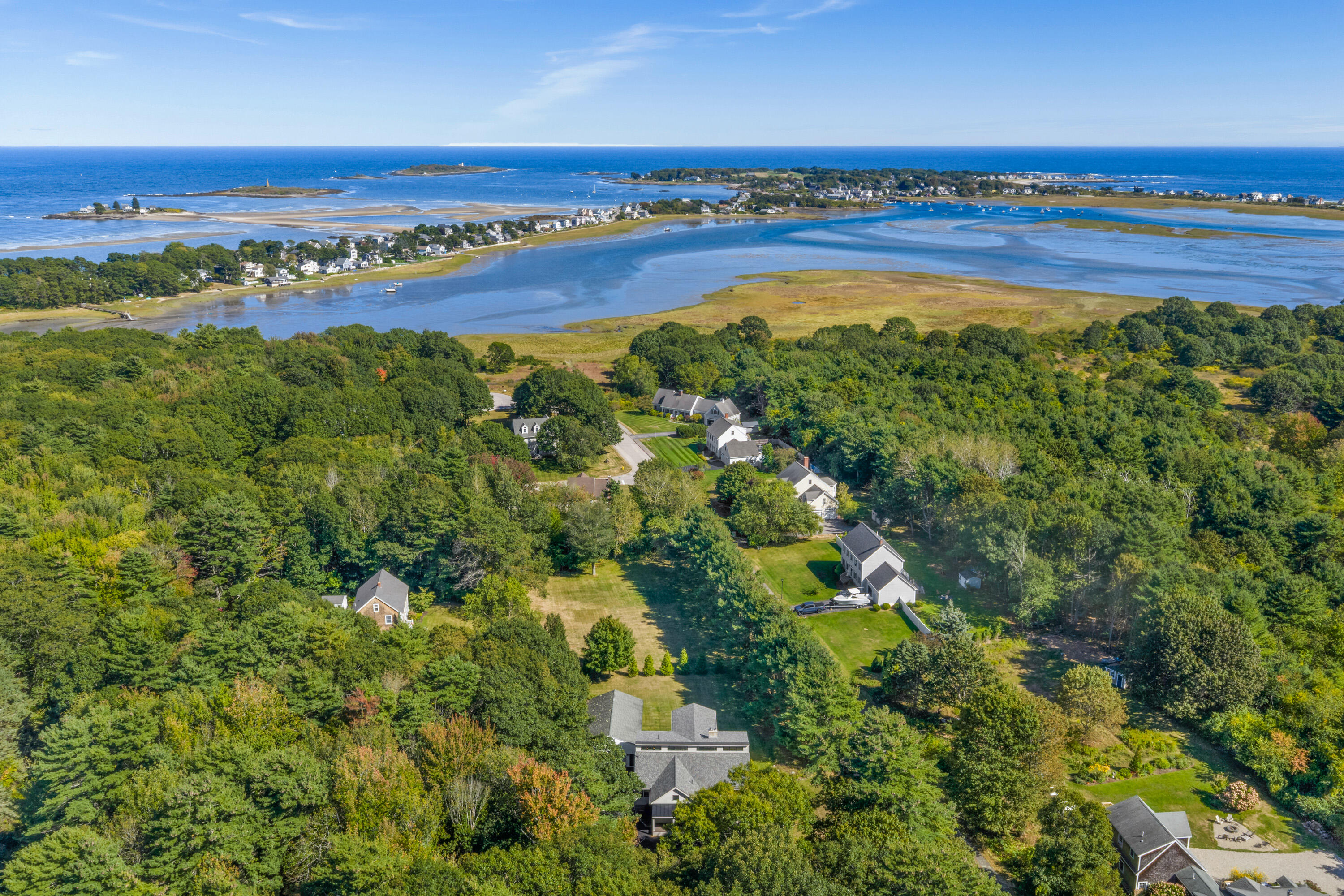 Aerial view of a wooded home beside coastal wetlands, with tidal water and ocean in the distance.