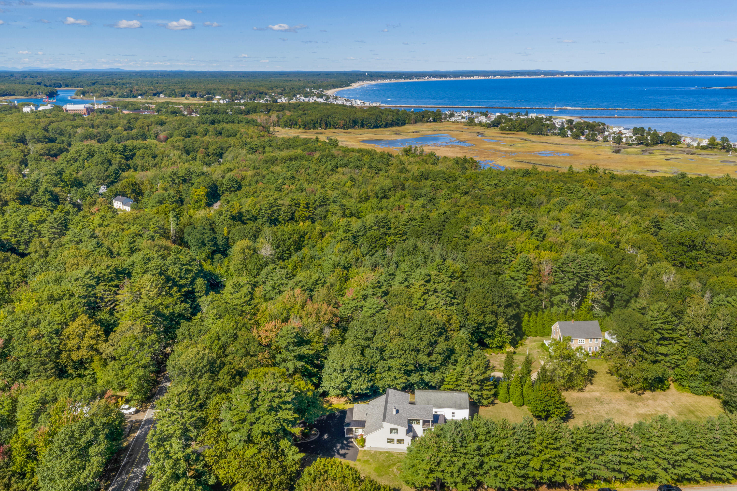 Aerial view of a home amid dense trees, with coastal marsh and ocean beyond.