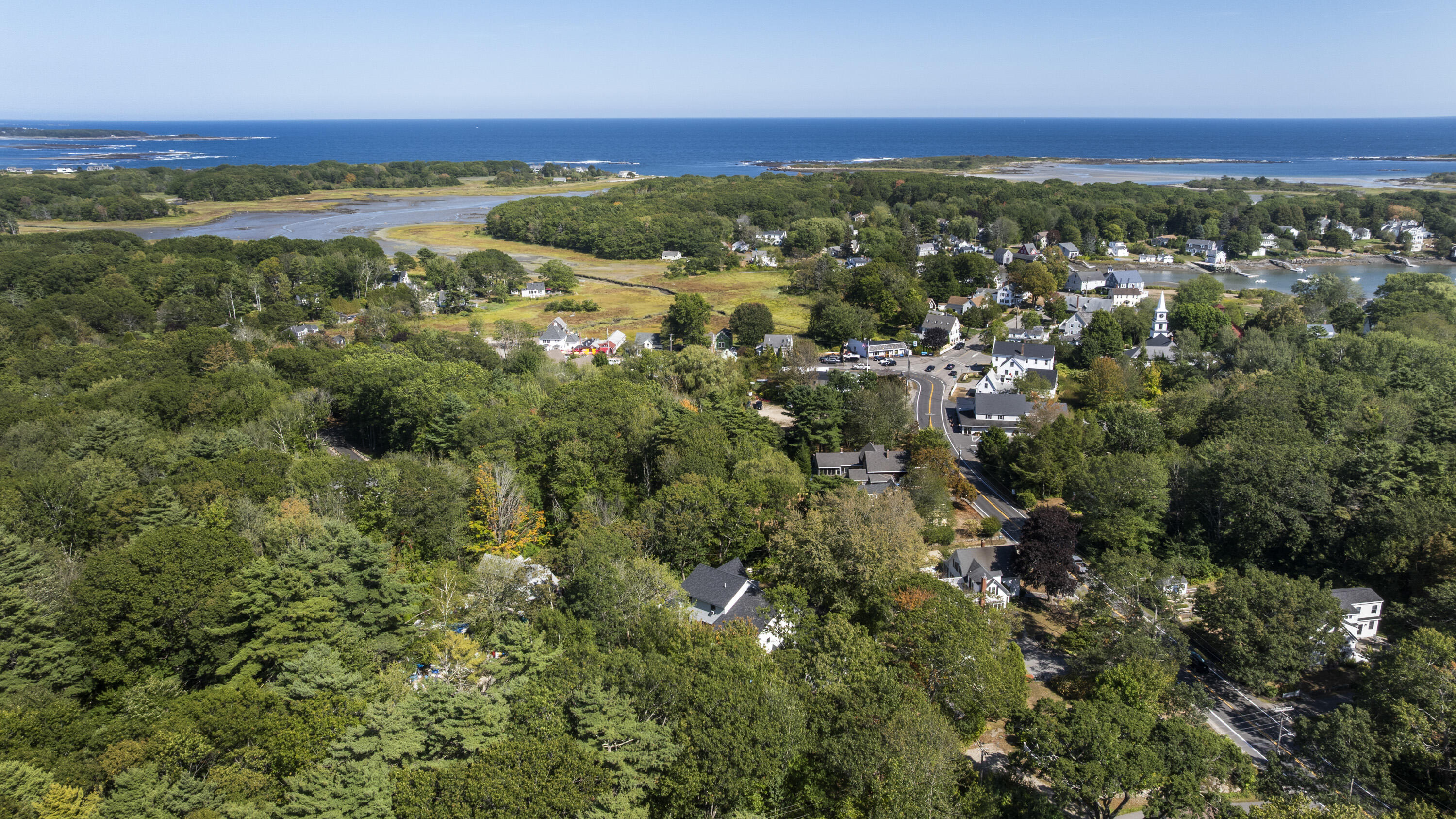 Aerial view of a wooded Kennebunkport village, tidal marshes, and ocean.