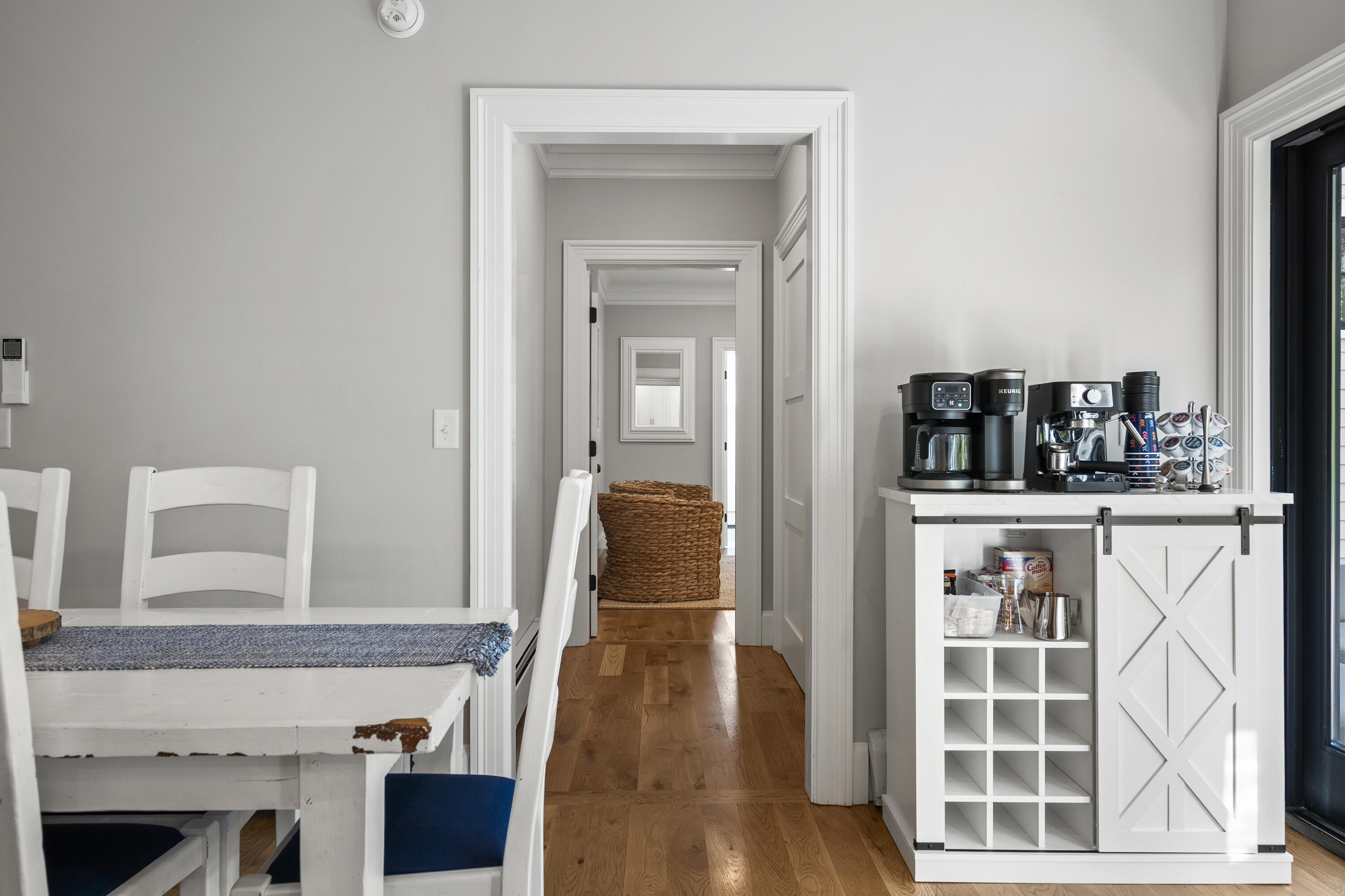 Dining area with a white coffee station beside a hallway with hardwood floors.