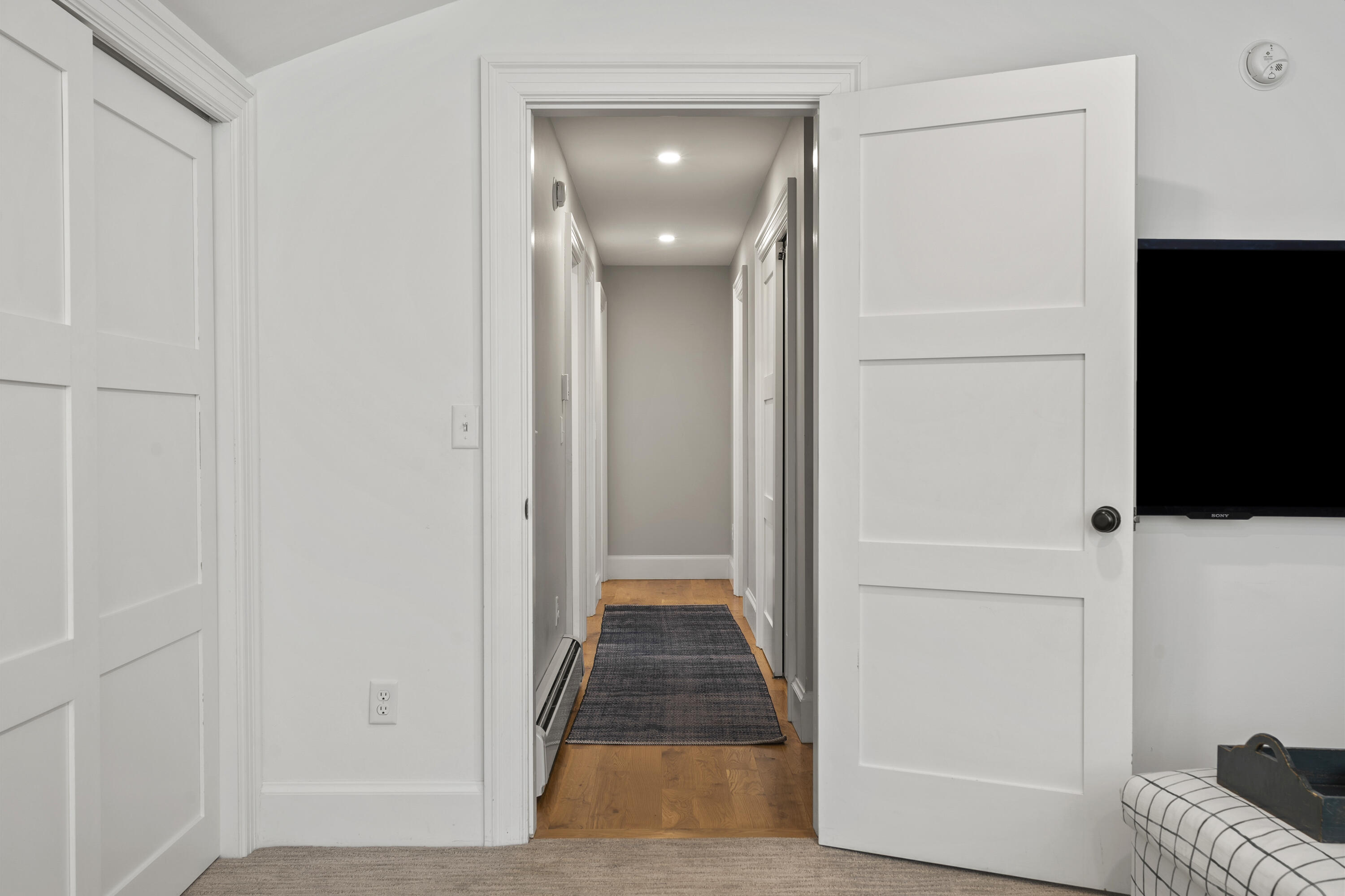 Hallway with hardwood floors, a dark runner rug, recessed lights, and white paneled doors.
