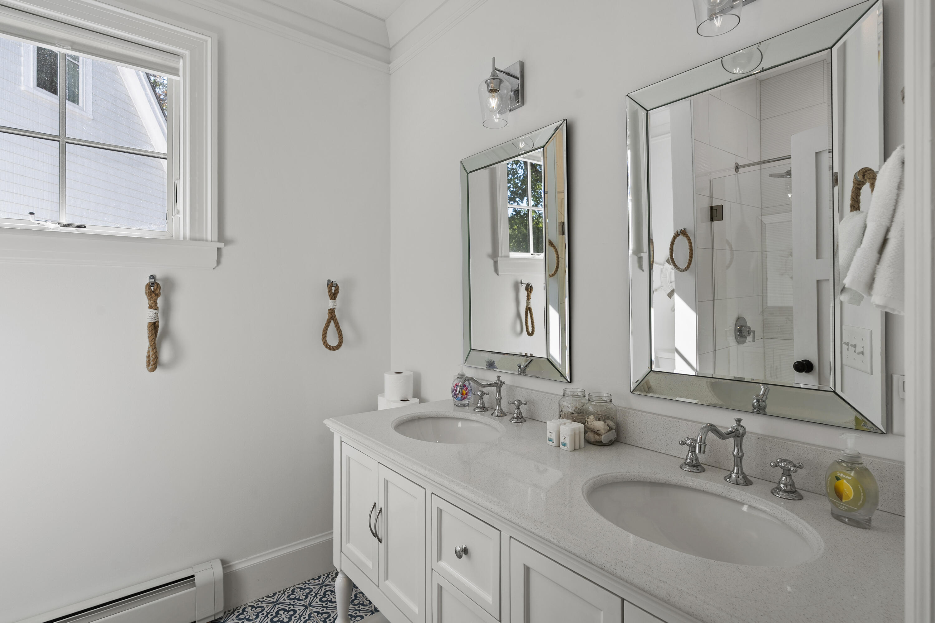 Bathroom with a double-sink vanity, mirrored cabinets, tiled shower, and blue-and-white patterned floor.