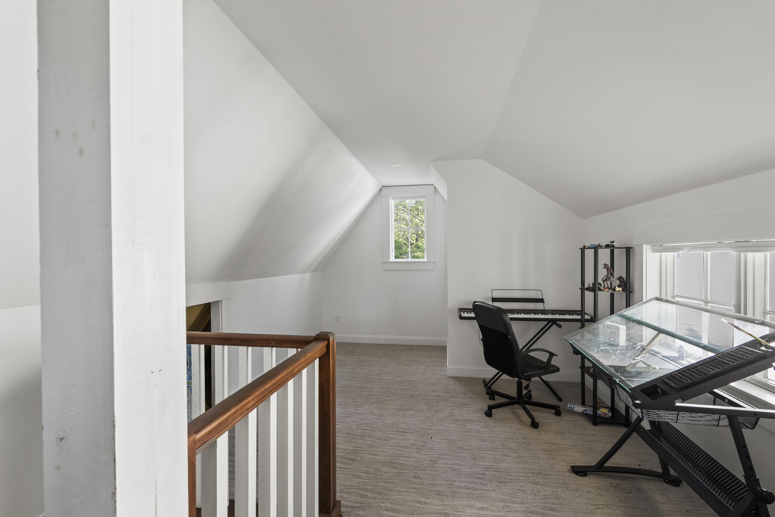 Upper-floor office with a sloped ceiling, digital keyboard, glass drafting table, and wooden stair railing.