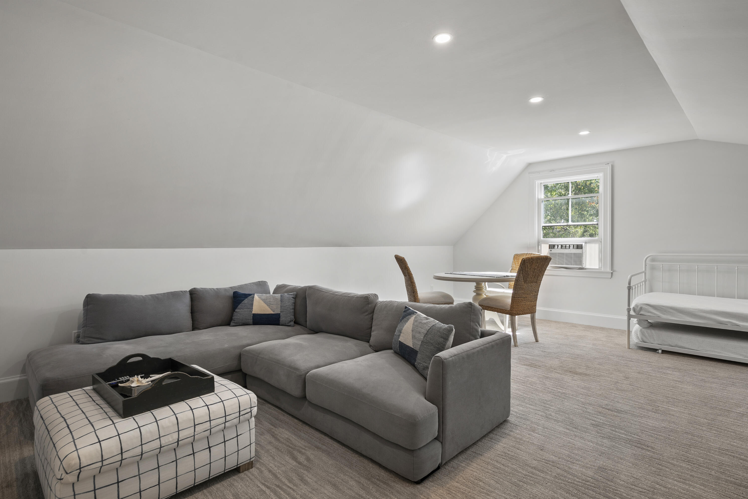 Upstairs living area with a gray sectional, patterned ottoman, dining table, and white daybed.