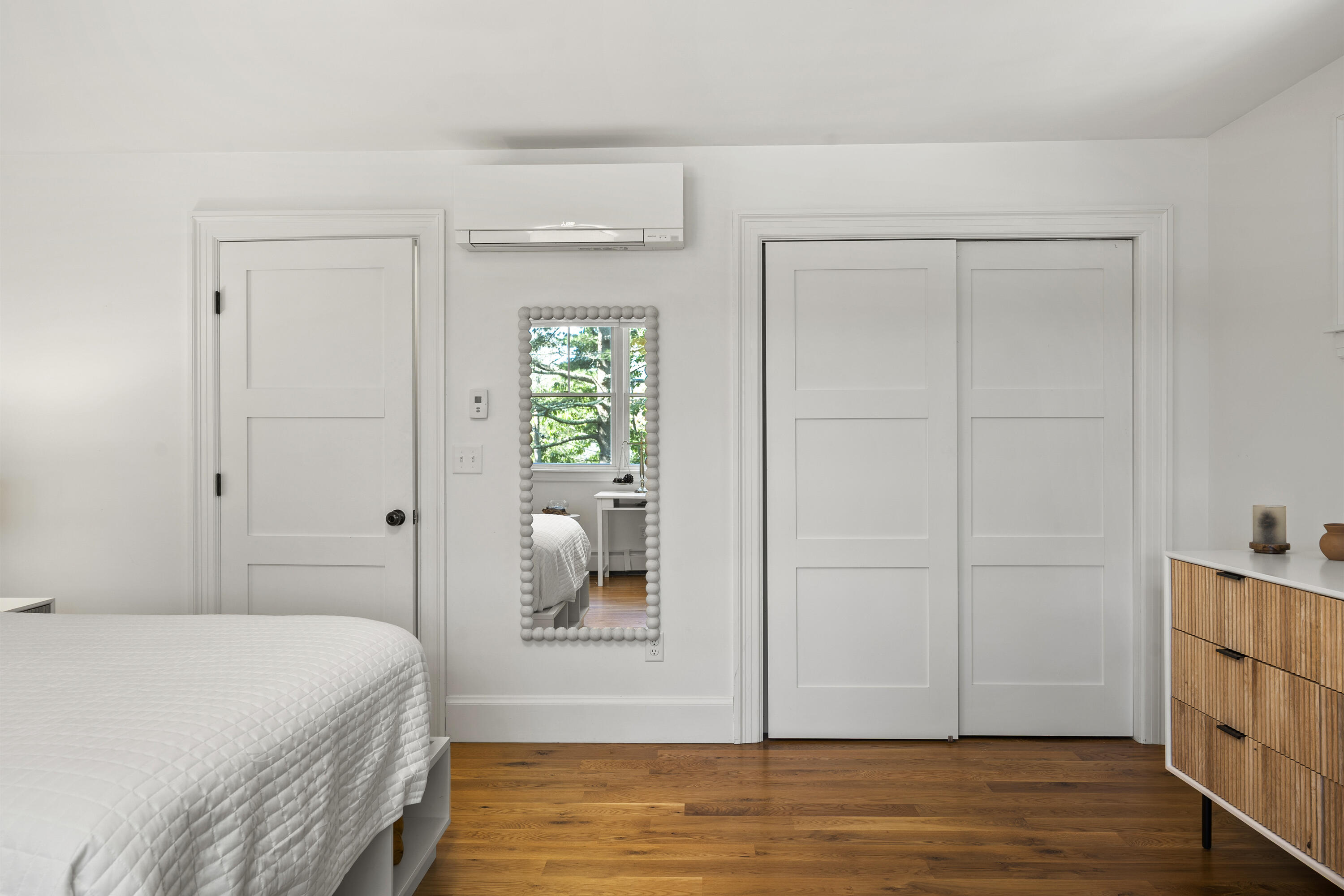 Bedroom with a white quilted bed, hardwood floors, sliding closet doors, and a bead-framed mirror.