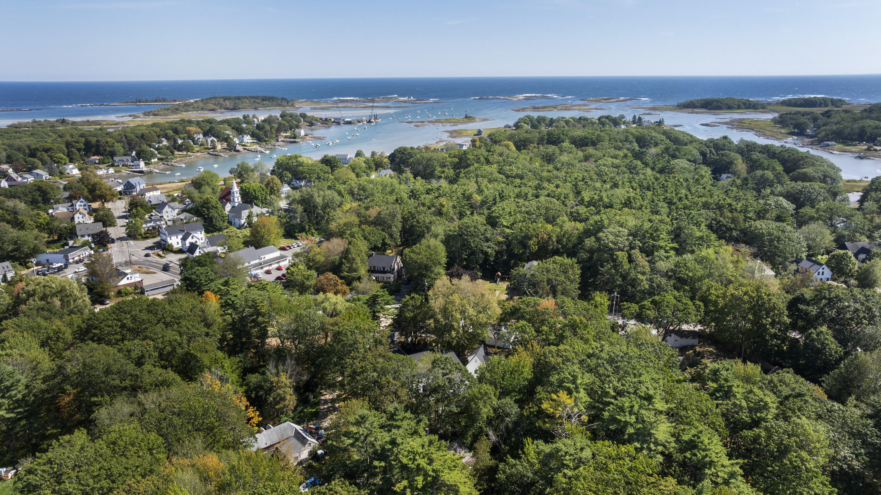 Aerial view of Kennebunkport’s harbor, boats, wooded neighborhood, and Atlantic coastline.