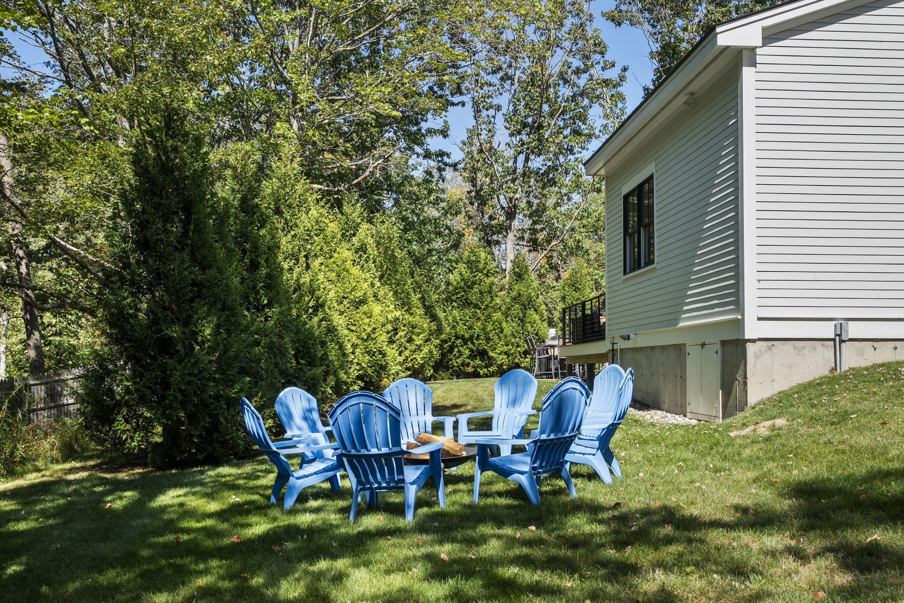 House rear yard with blue Adirondack chairs arranged around a small table beneath leafy trees.