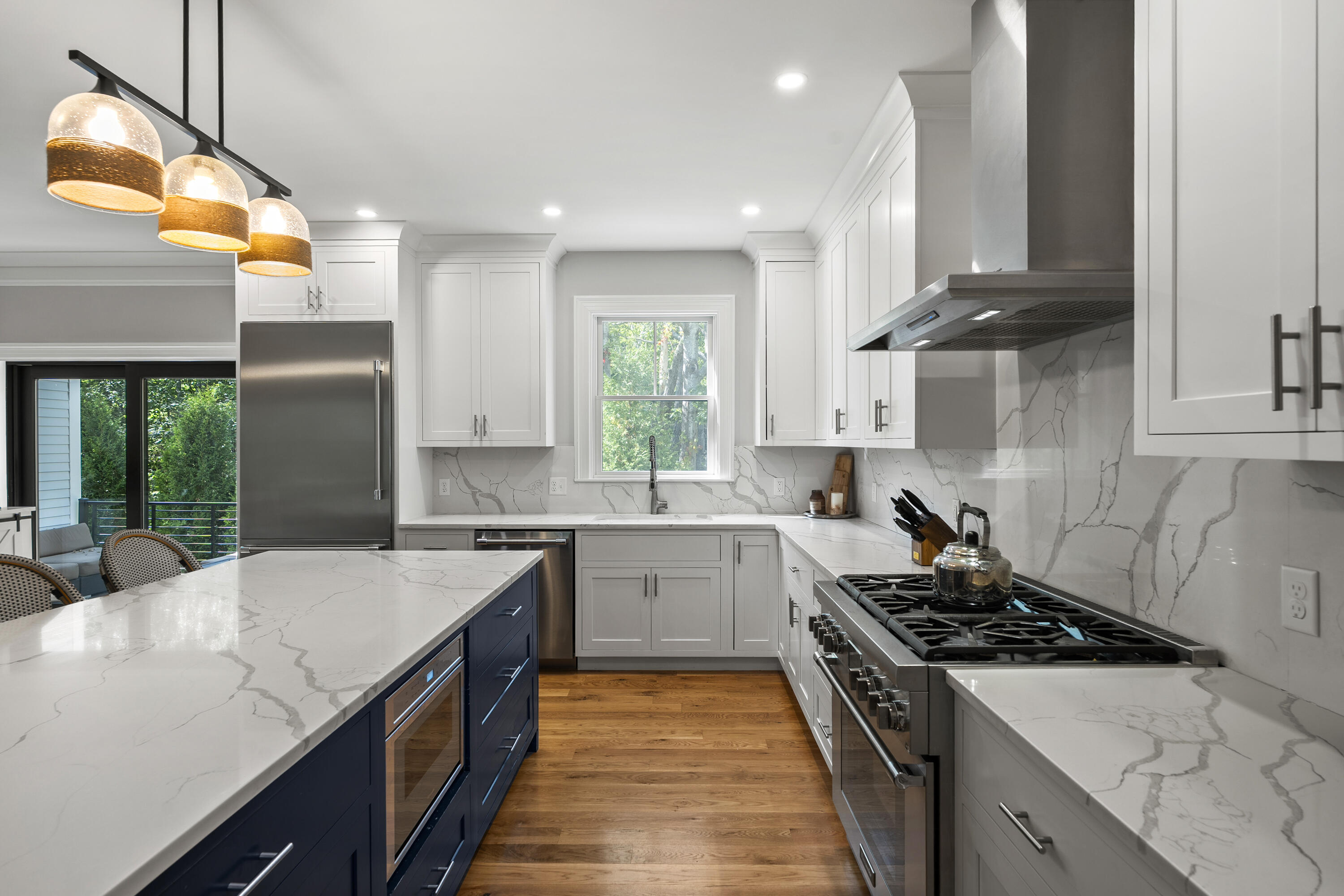 Renovated kitchen with a navy island, veined countertops, stainless steel range, and three pendant lights.