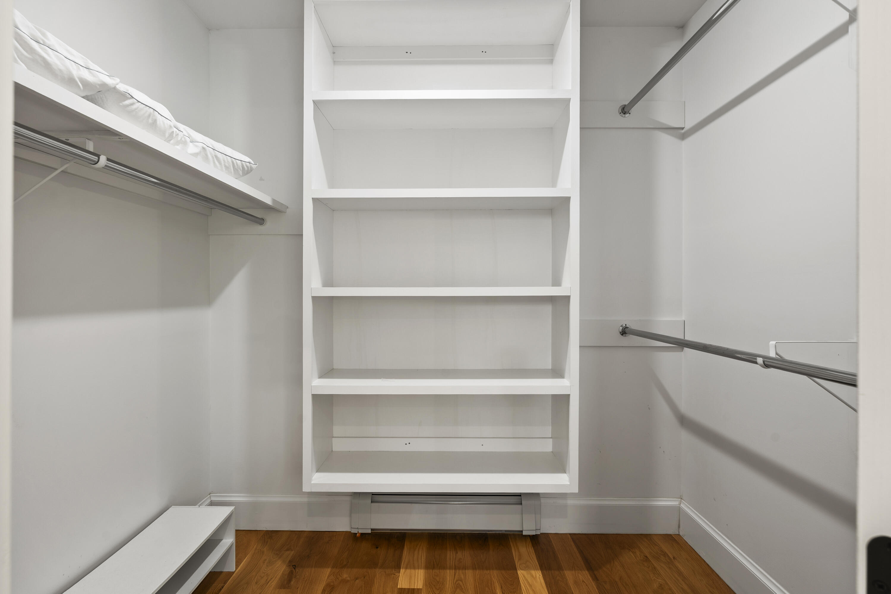 Walk-in closet with central white shelving, hanging rods on both sides, and hardwood flooring.