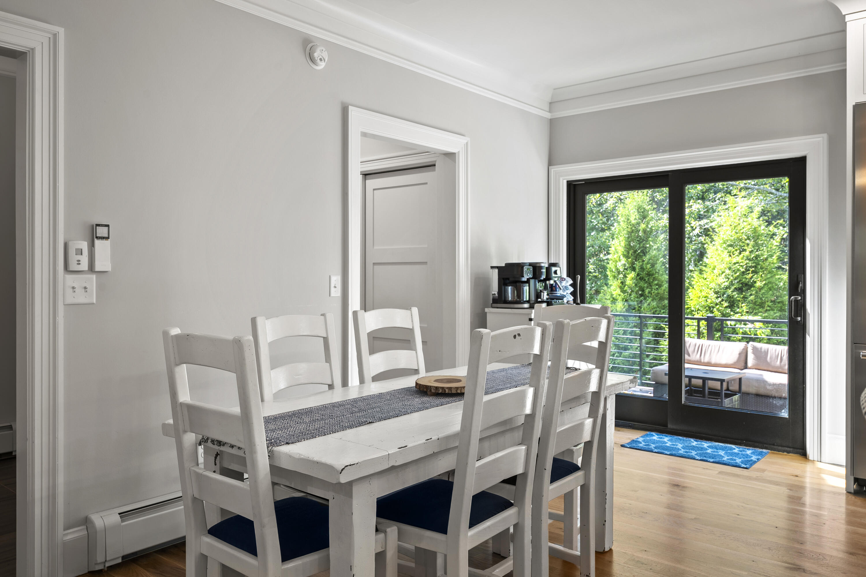 Dining room with a white farmhouse table beside sliding glass doors to a leafy balcony.