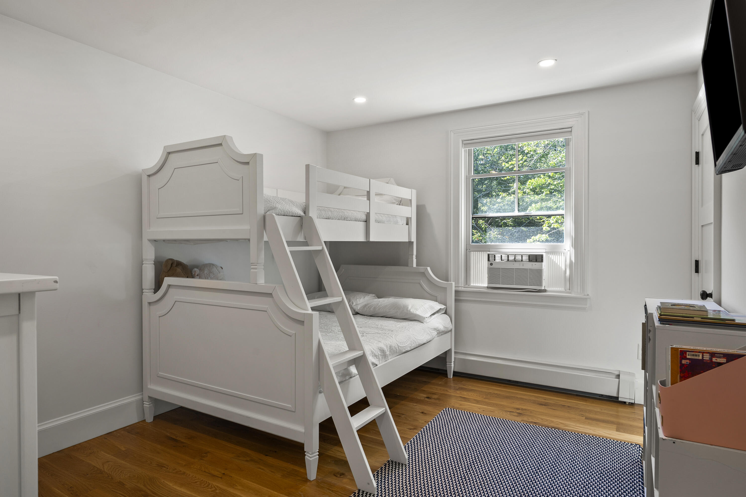 Bedroom with a white bunk bed, hardwood floors, and a window air conditioner.