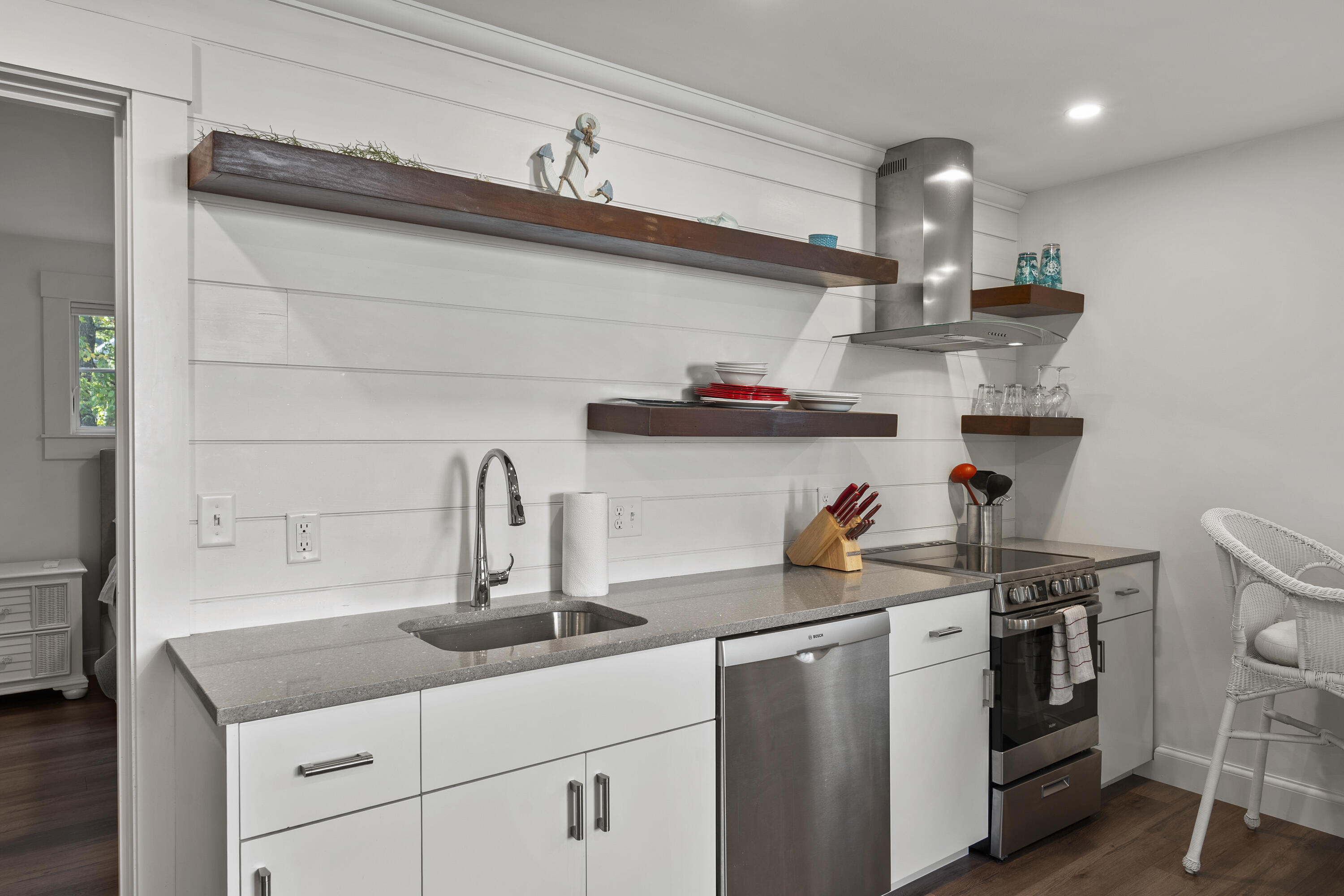 Kitchen with white cabinetry, gray counters, stainless steel appliances, and dark floating shelves.