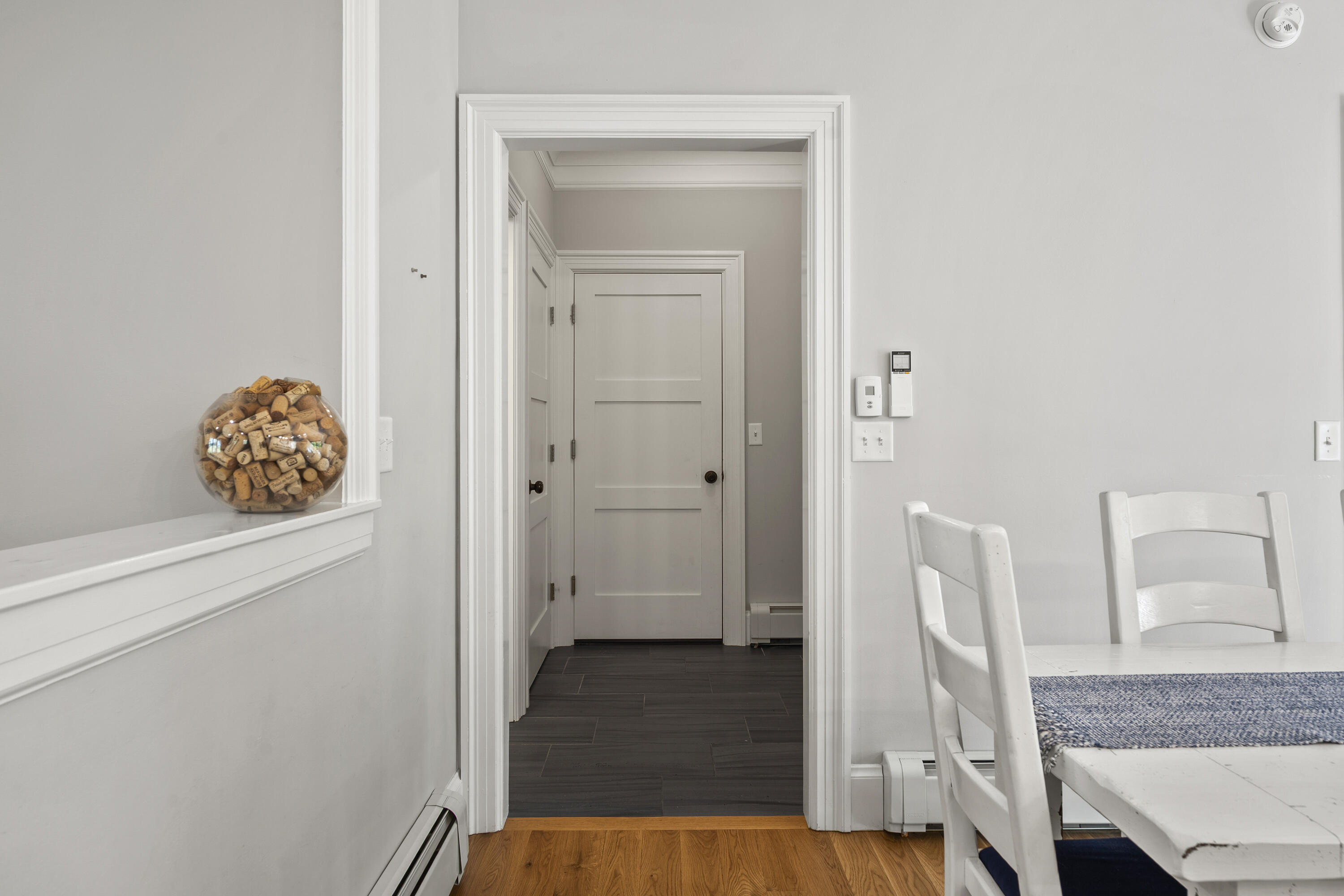 White dining area with a blue table runner, opening onto a dark-tiled hallway.