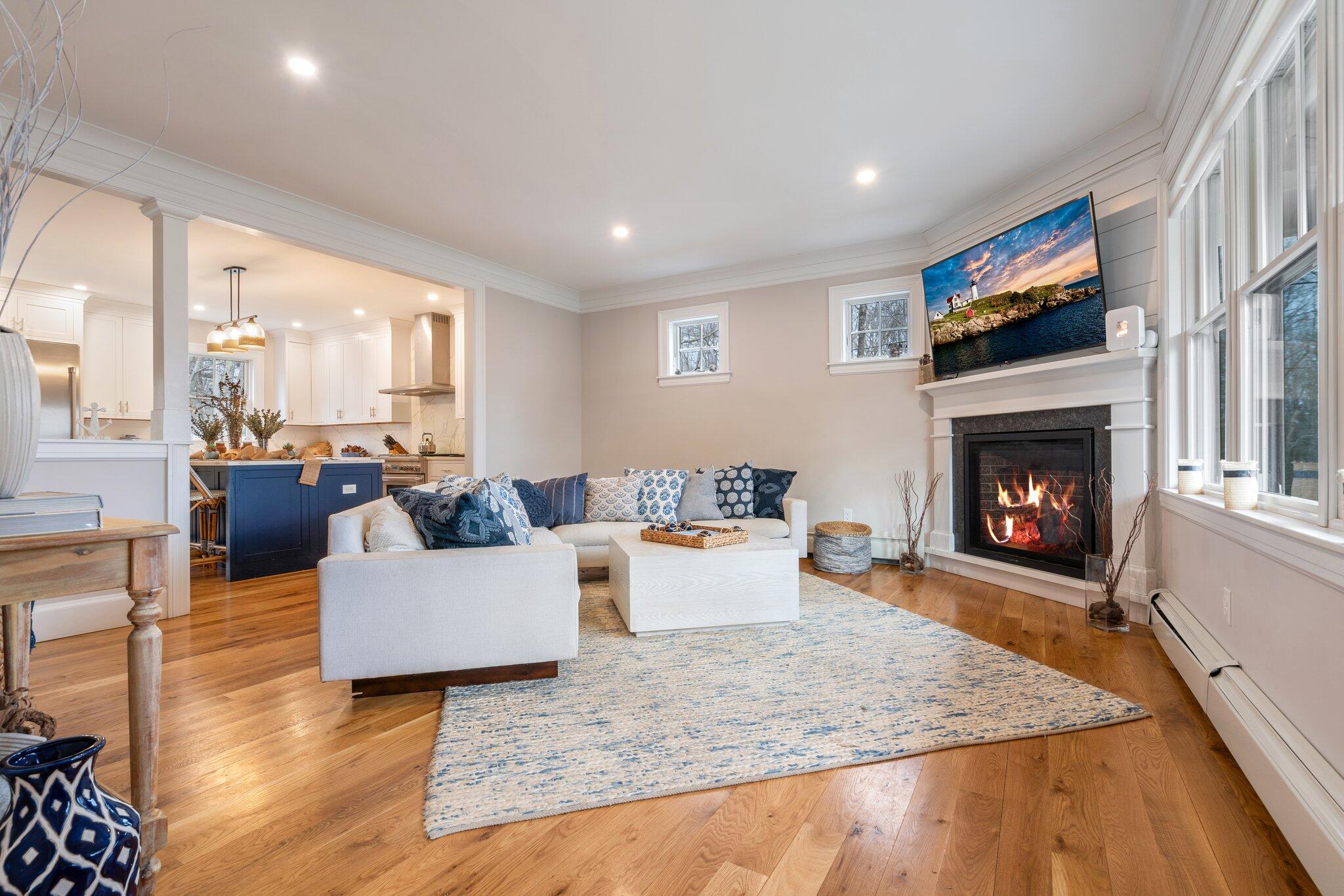 Living room with a lit fireplace, hardwood floors, and an open kitchen with a blue island.