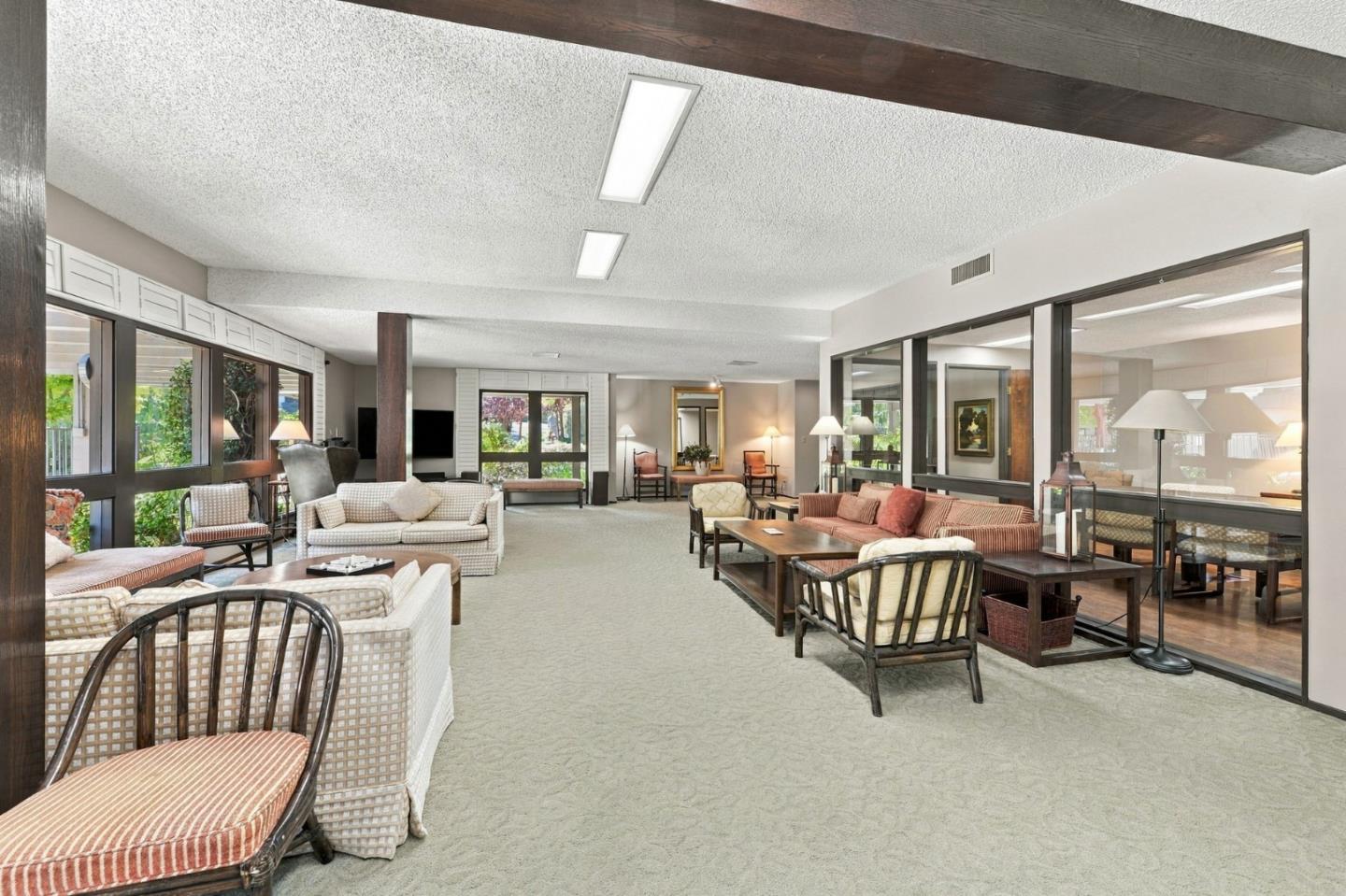 Communal lounge with sofas and chairs around coffee tables, beside large windows and glass partitions.