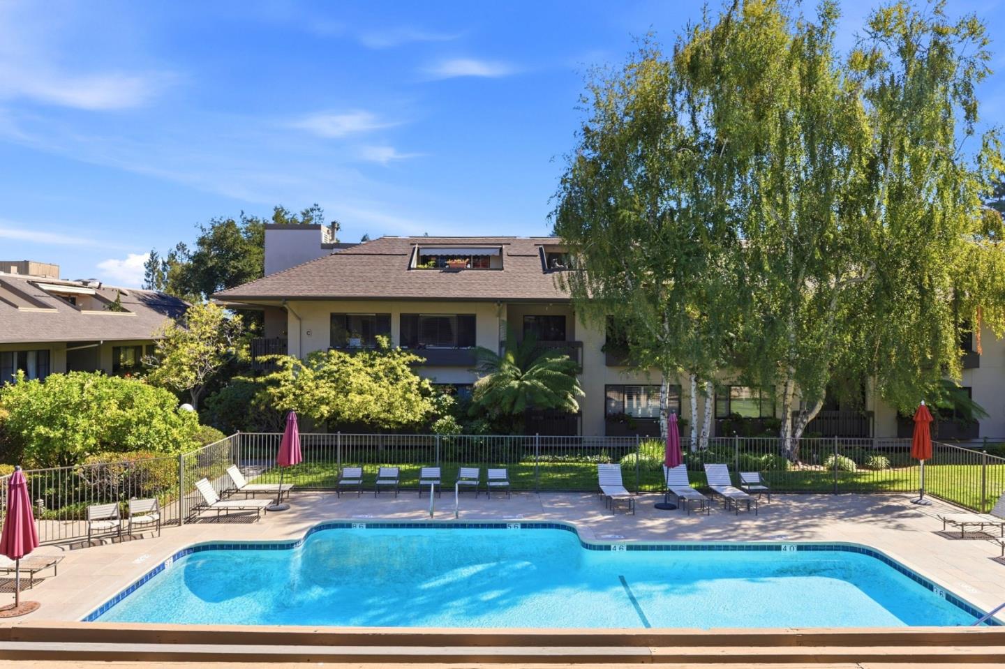 Condominium pool with lounge chairs and umbrellas in front of a landscaped residential building.