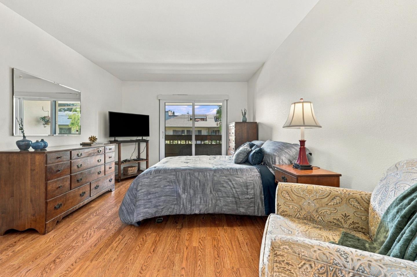 Bedroom with a gray-covered bed, hardwood floors, and sliding glass doors to a balcony.
