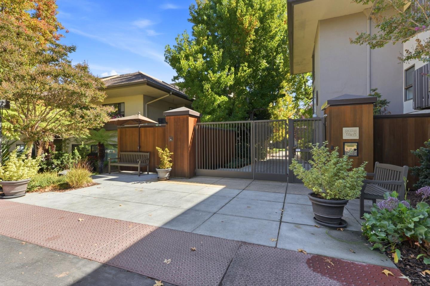 Condominium entrance with a metal gate, wood-paneled posts, and benches beside the walkway.
