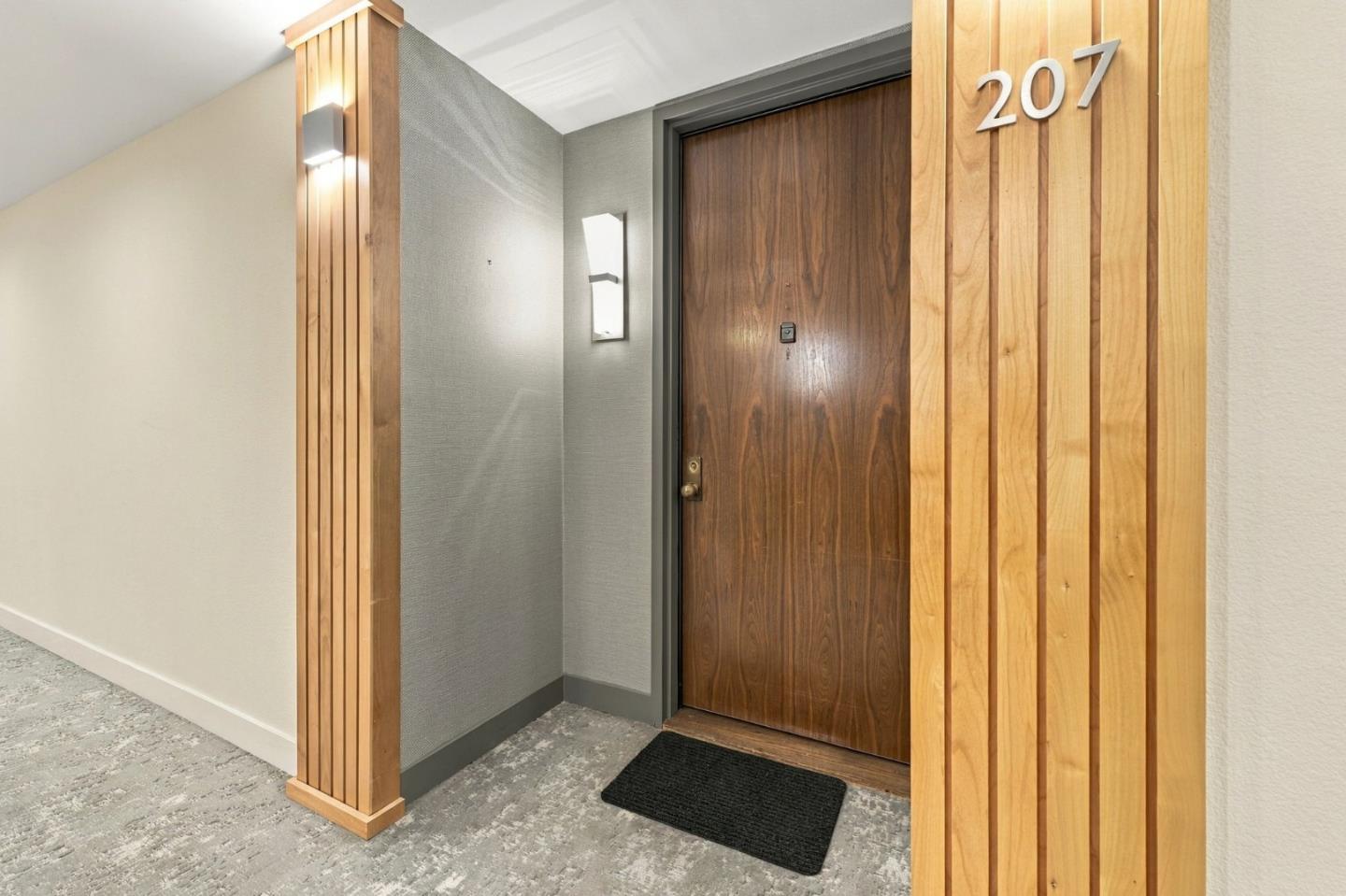 Condominium entry door numbered 207, framed by vertical wood paneling in a carpeted hallway.
