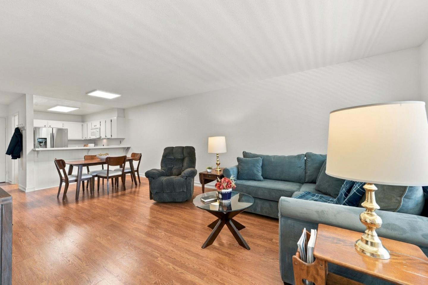 Open-plan condo living and dining room with teal seating, hardwood floors, and a white kitchen.