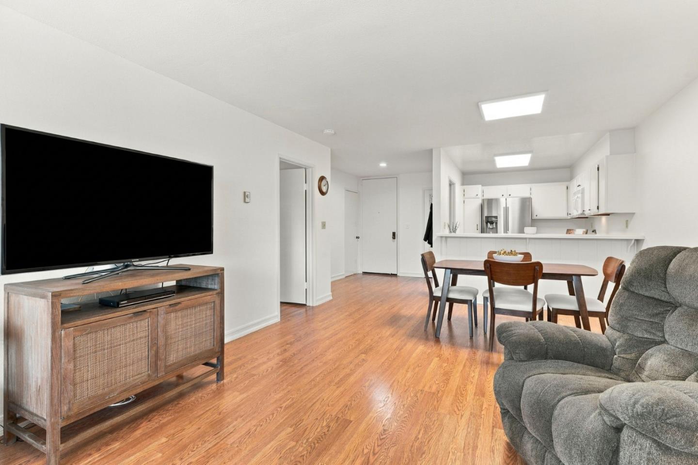 Open-plan living and dining area with hardwood floors, a gray recliner, and a kitchen with stainless steel appliances.