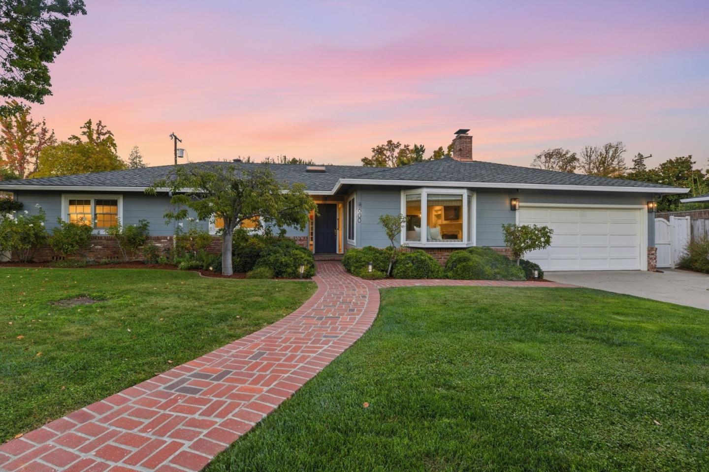Single-story house with a curved brick walkway, front lawn, and attached garage at dusk.