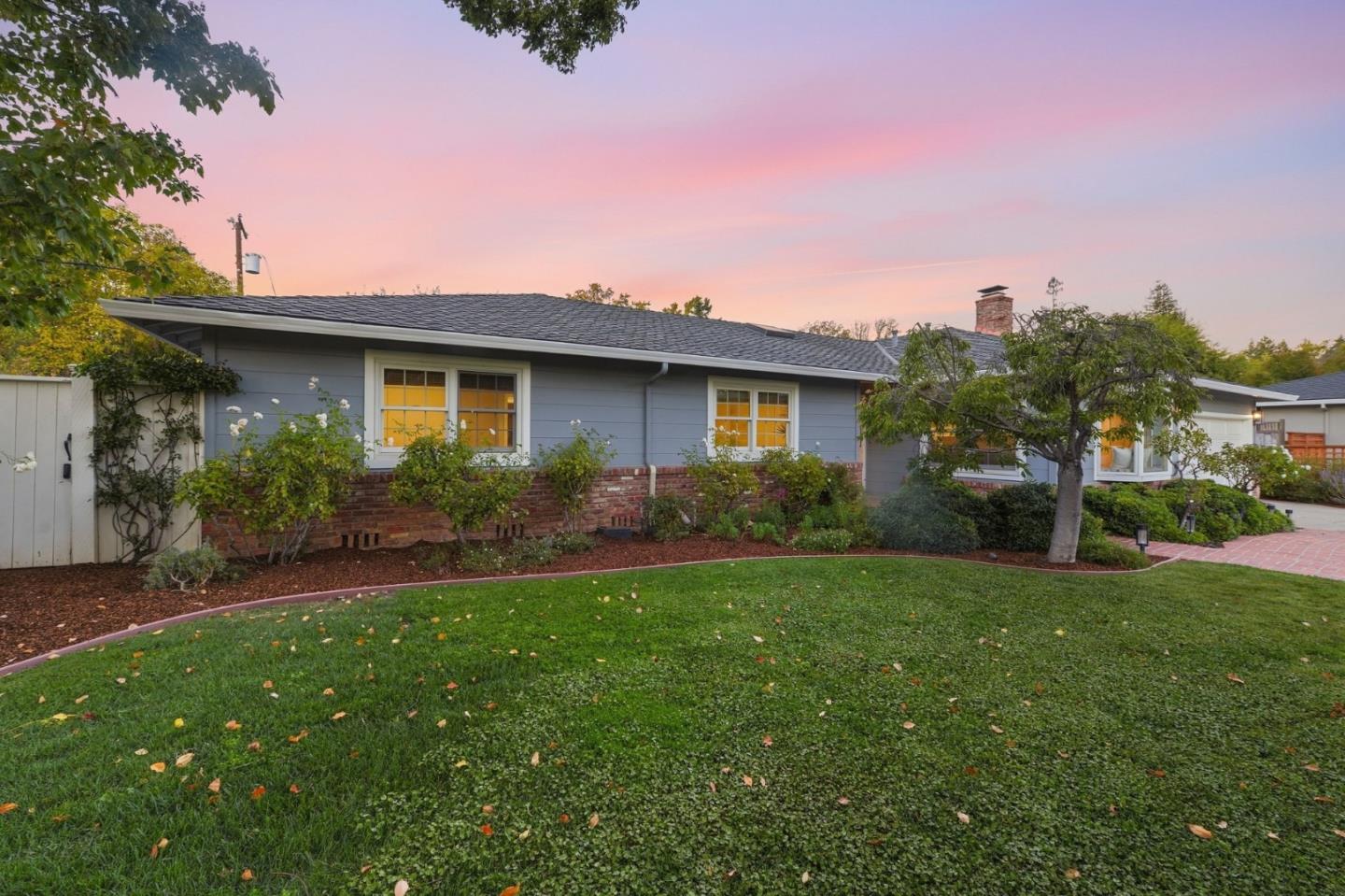 Single-story gray house with brick trim, landscaped garden, and broad lawn at dusk.