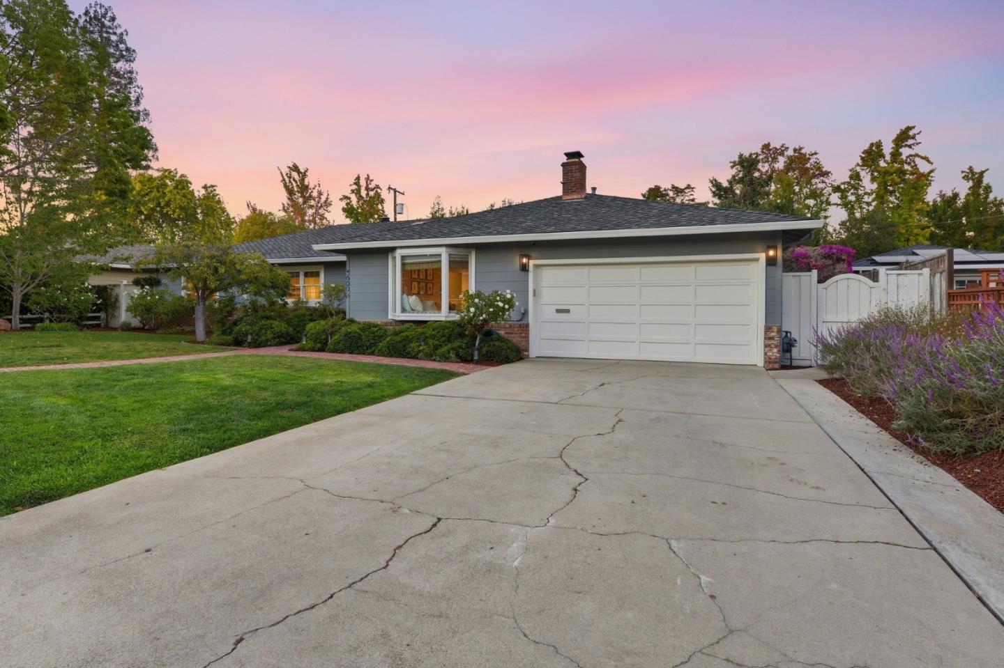 Gray single-story home with a white double garage, broad driveway, and pink dusk sky.