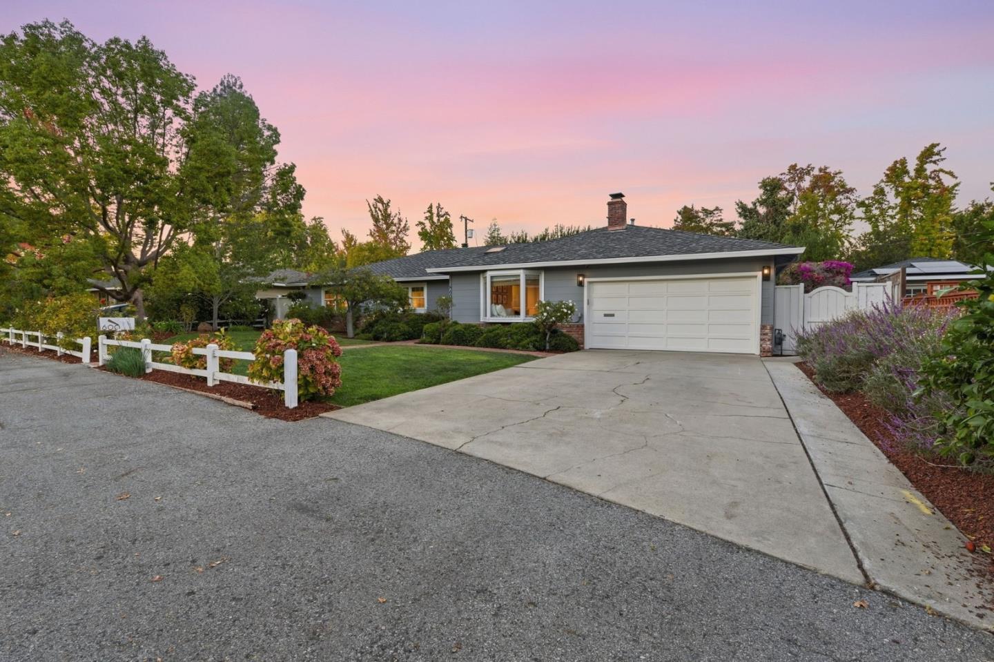 Single-story gray house with a white garage, broad driveway, and landscaped front yard at dusk.