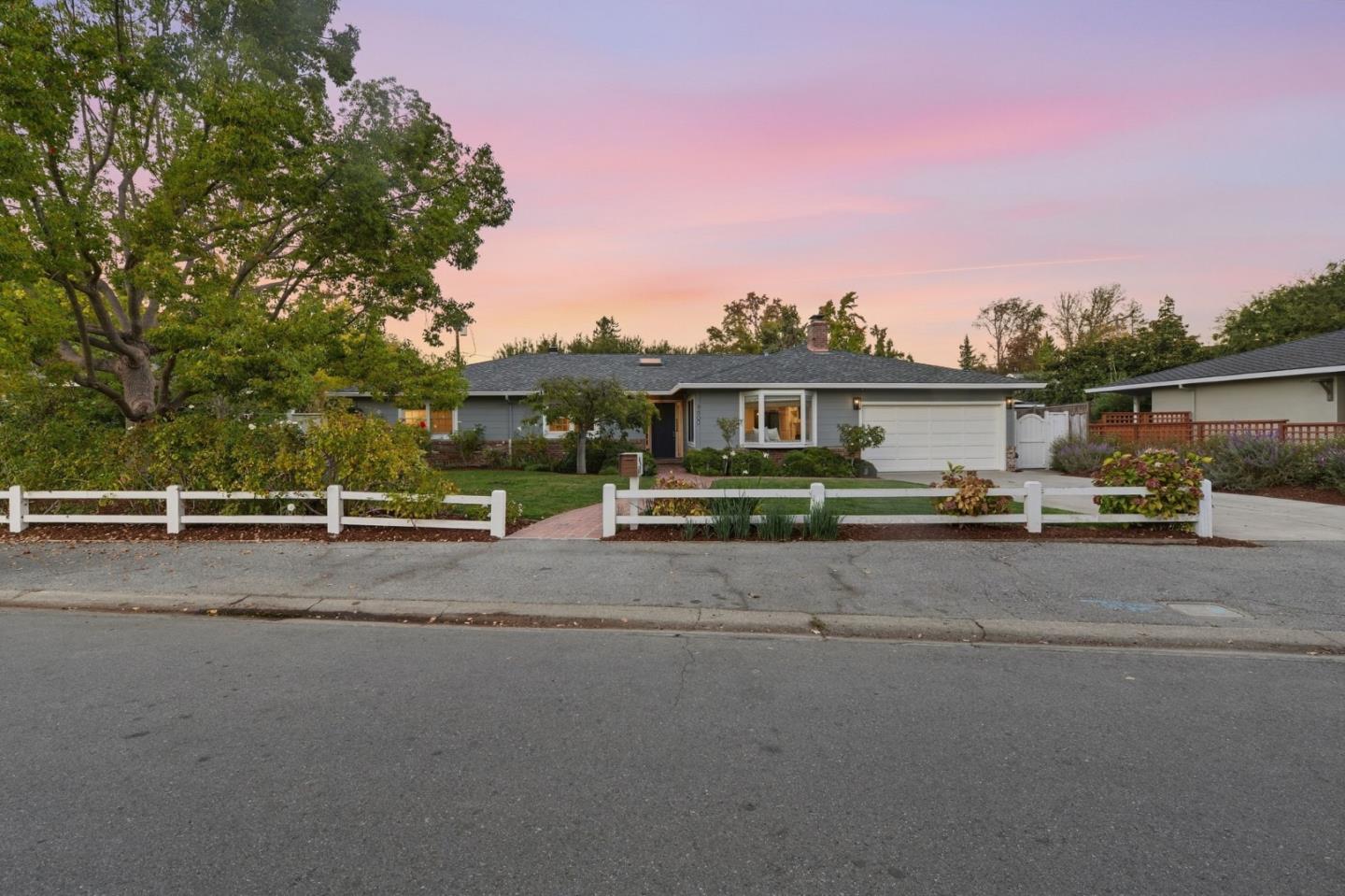 Single-story gray home with a white garage door and landscaped yard at dusk.