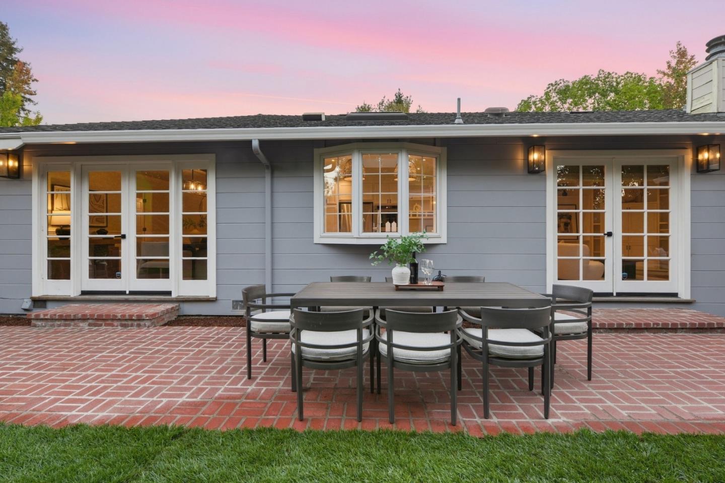 Home’s rear patio with a brick terrace, outdoor dining set, French doors, and gray siding.