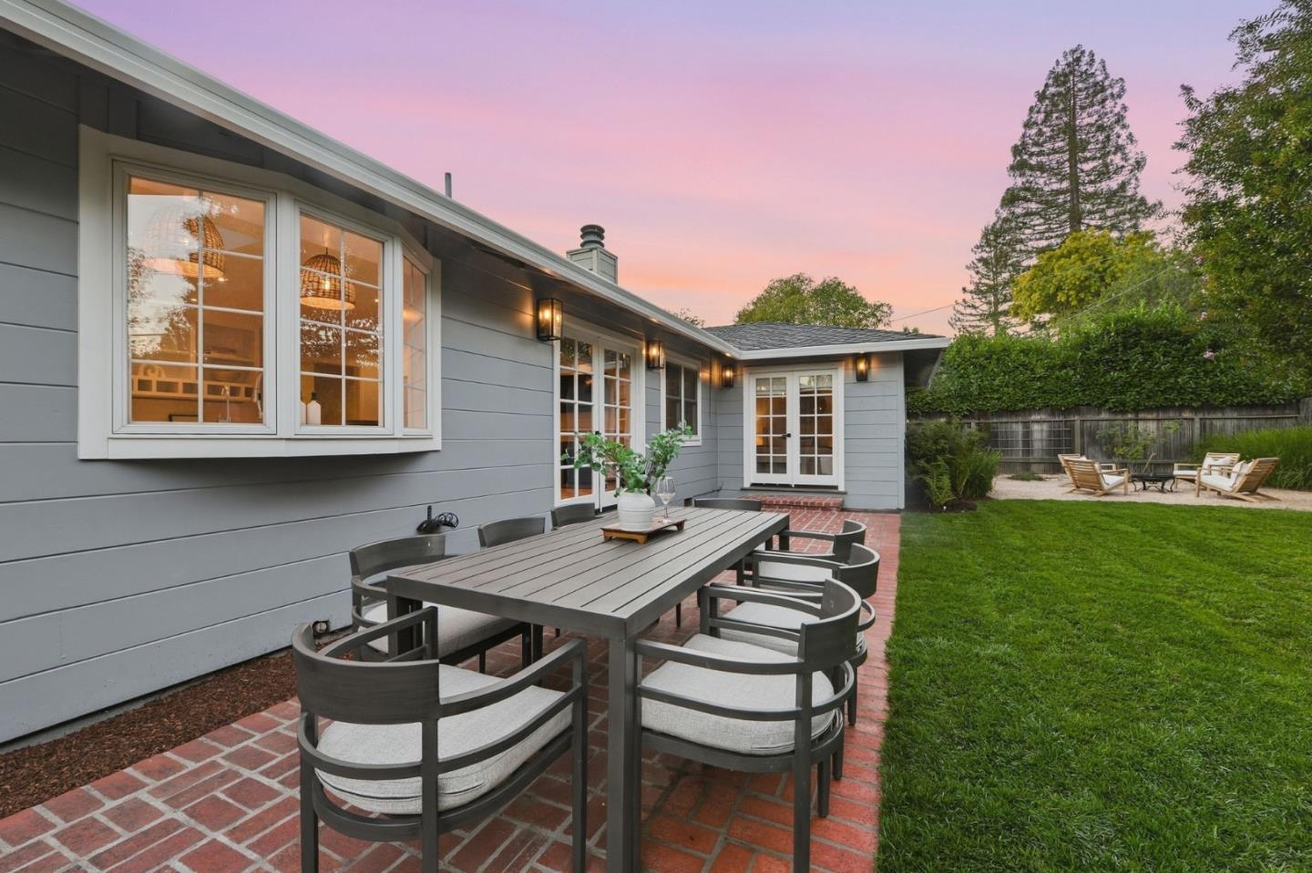 Home’s backyard patio with a brick dining area, lawn, and outdoor seating at dusk.
