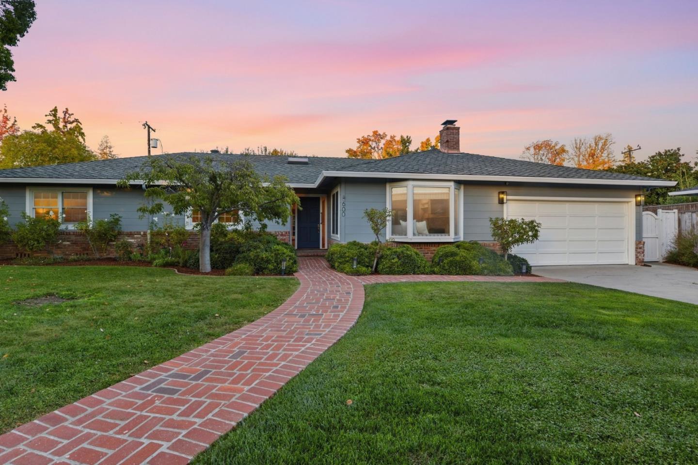 Single-story home with blue-gray siding, an attached garage, and a curved brick walkway at dusk.