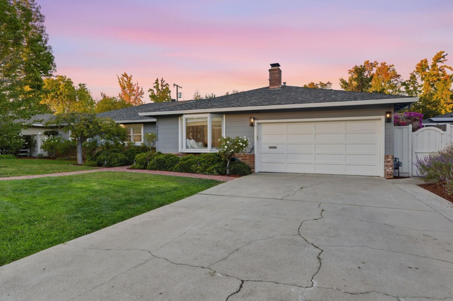 Single-story gray home with a white double garage, broad driveway, and green front lawn at dusk.