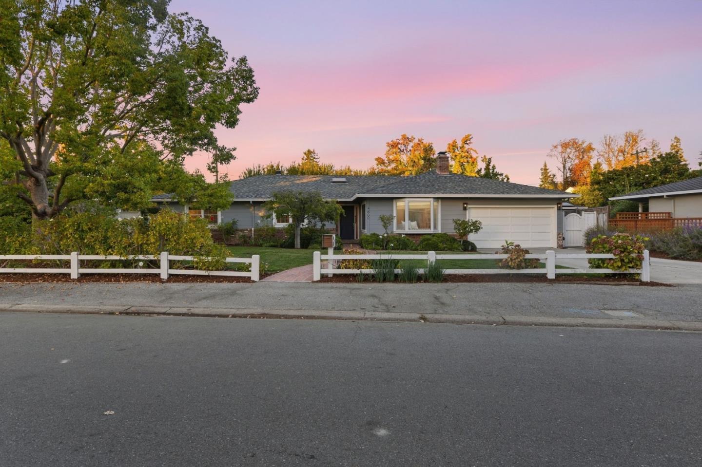 Single-story gray home with a white garage door and fence at dusk.