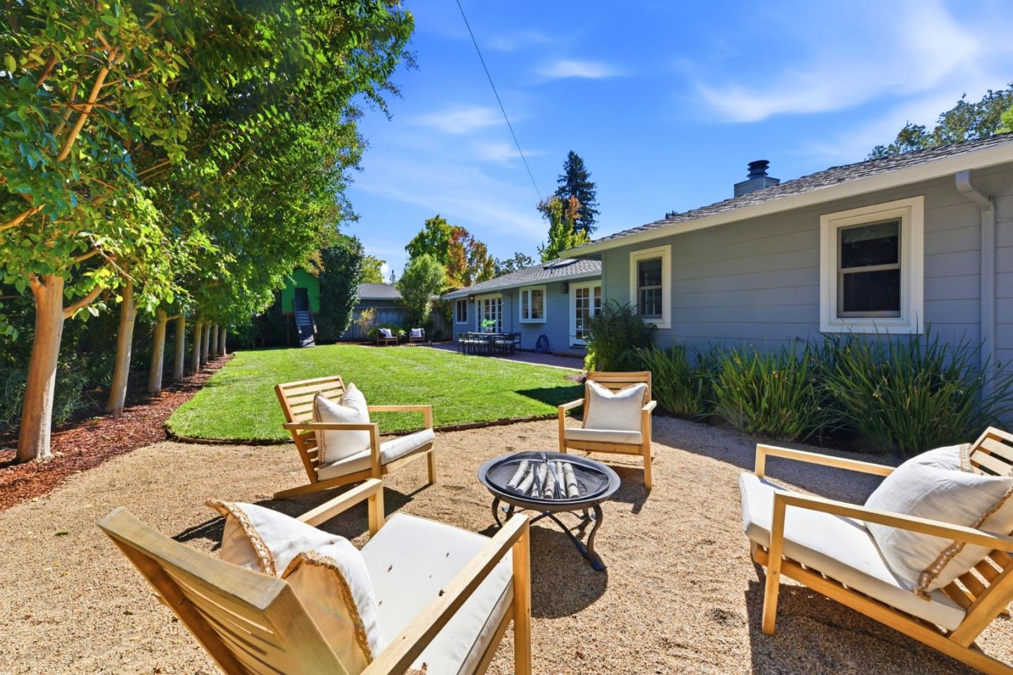 Backyard patio with cushioned chairs around a fire pit beside a green lawn.