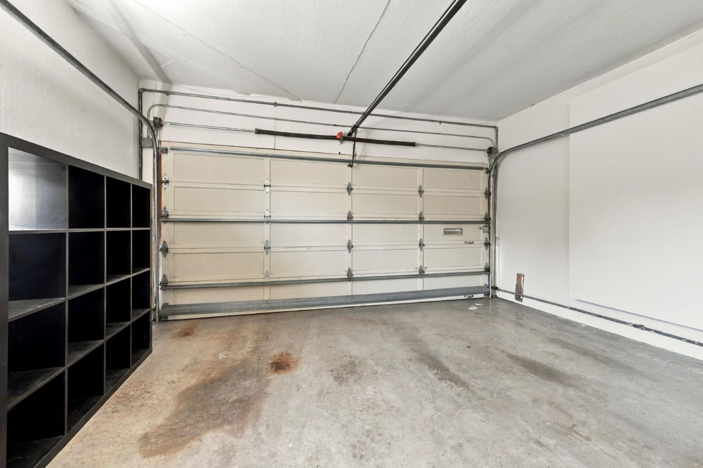 Empty garage with a closed sectional door, concrete floor, and black cubby shelving.