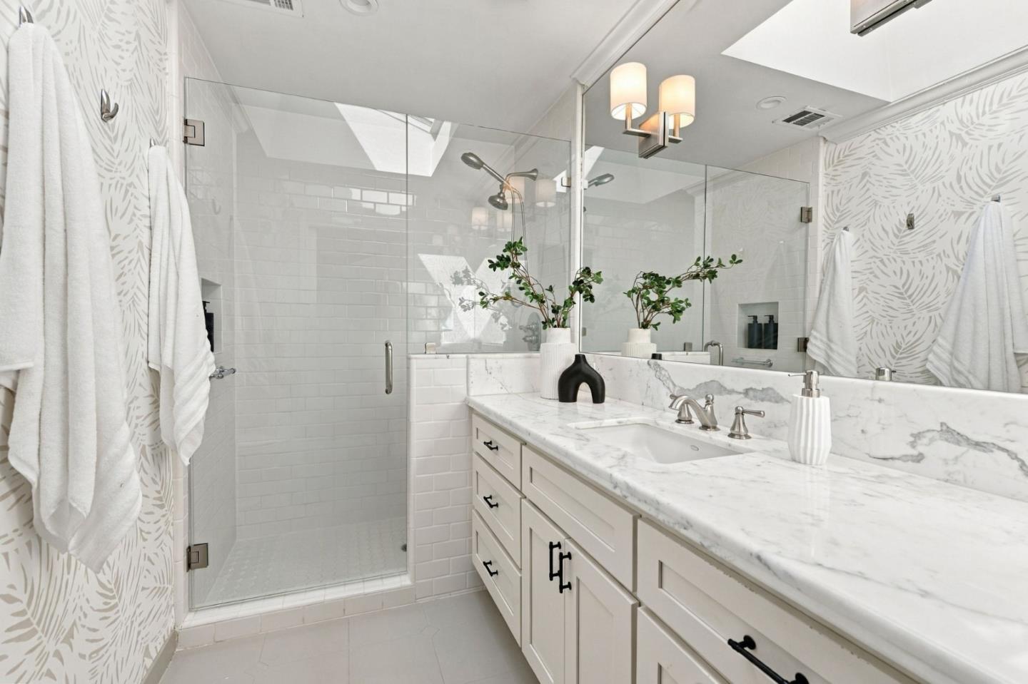 Bathroom with a glass shower, marble-topped vanity, and patterned wallpaper.