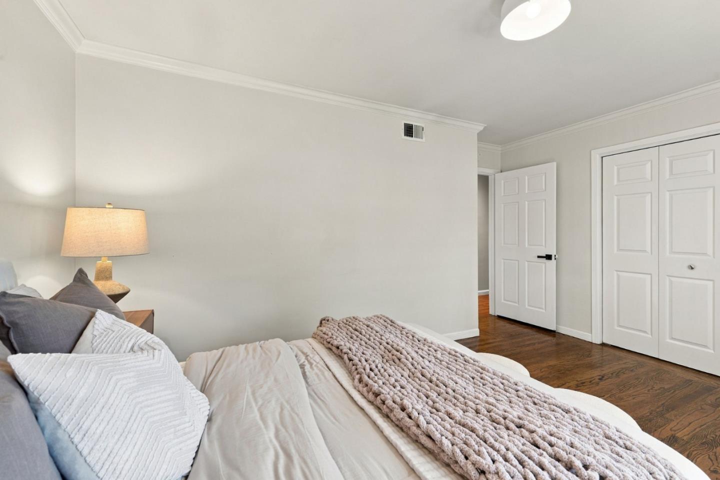 Bedroom with layered white and gray bedding, a chunky knit throw, and dark wood floors.