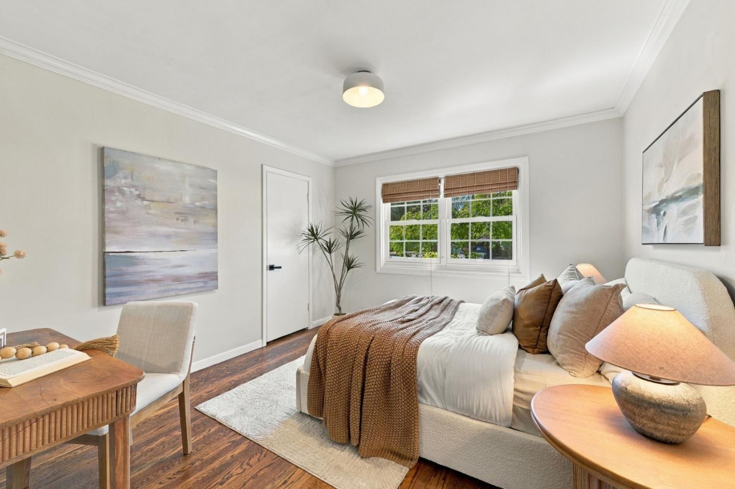 Staged bedroom with a white bed, brown throw, hardwood floors, and a window with woven shades.