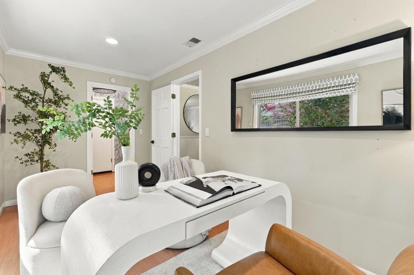 Home office with a sculptural white desk, upholstered chairs, and a large black-framed mirror.