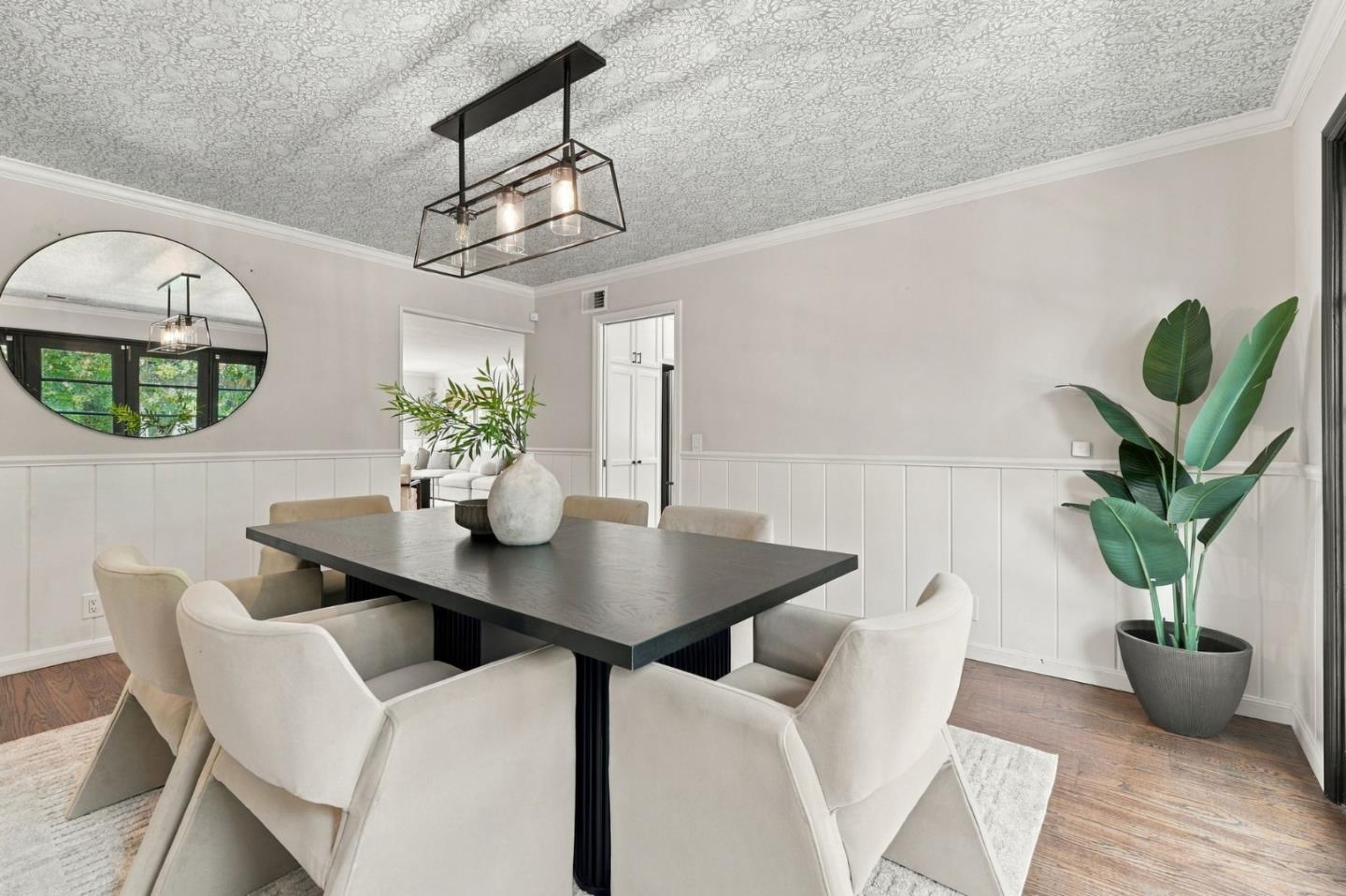 Dining room with a dark table, cream chairs, patterned ceiling, and large potted plant.