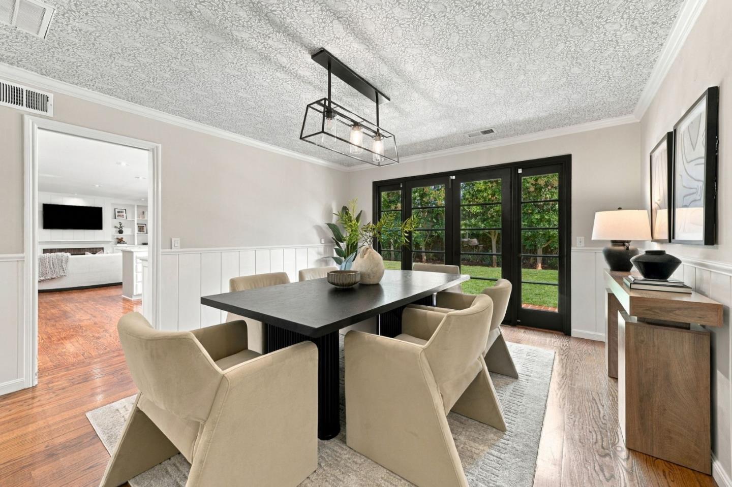 Staged dining room with a black table, cream chairs, and black-framed garden doors.