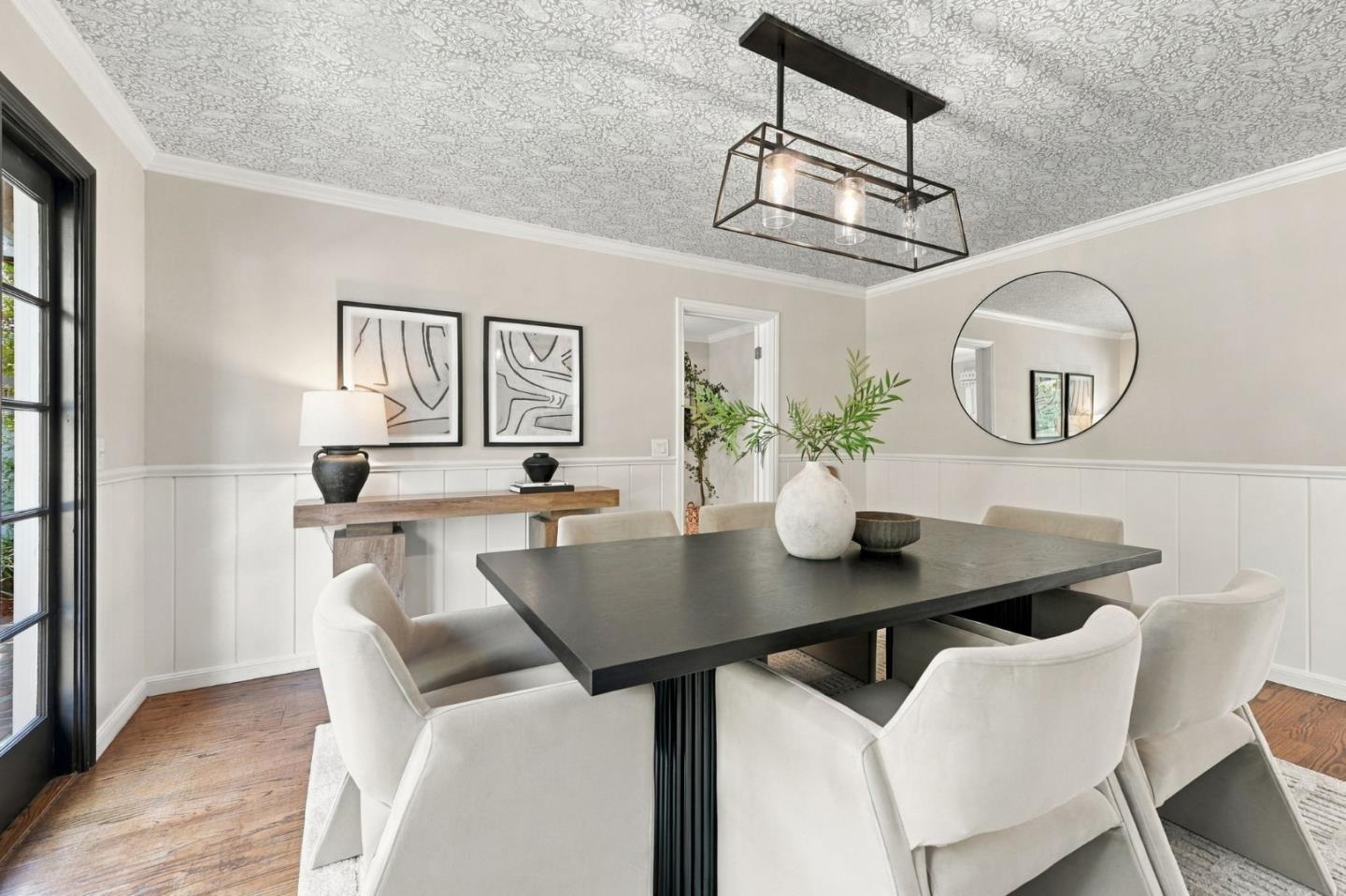 Dining room with a dark table, white upholstered chairs, patterned ceiling, and wood floors.