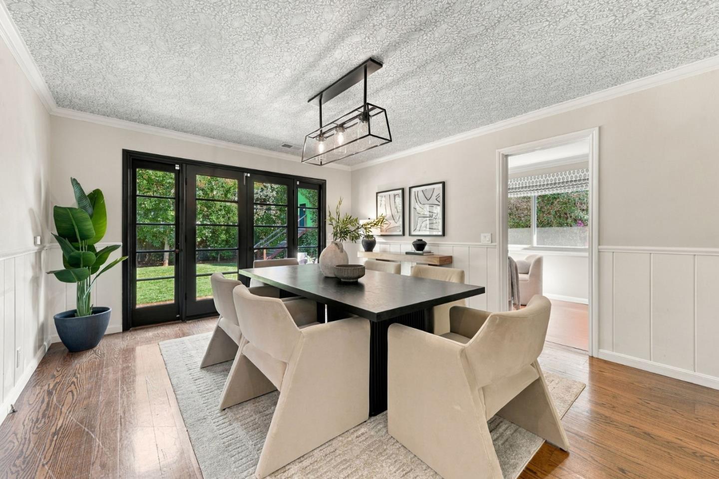 Dining room with a dark table, upholstered chairs, black-framed garden doors, and a patterned ceiling.