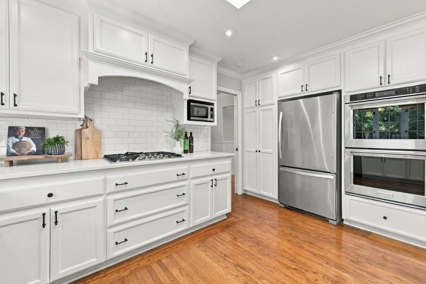 Bright kitchen with white cabinetry, stainless steel appliances, subway-tile backsplash, and hardwood floors.